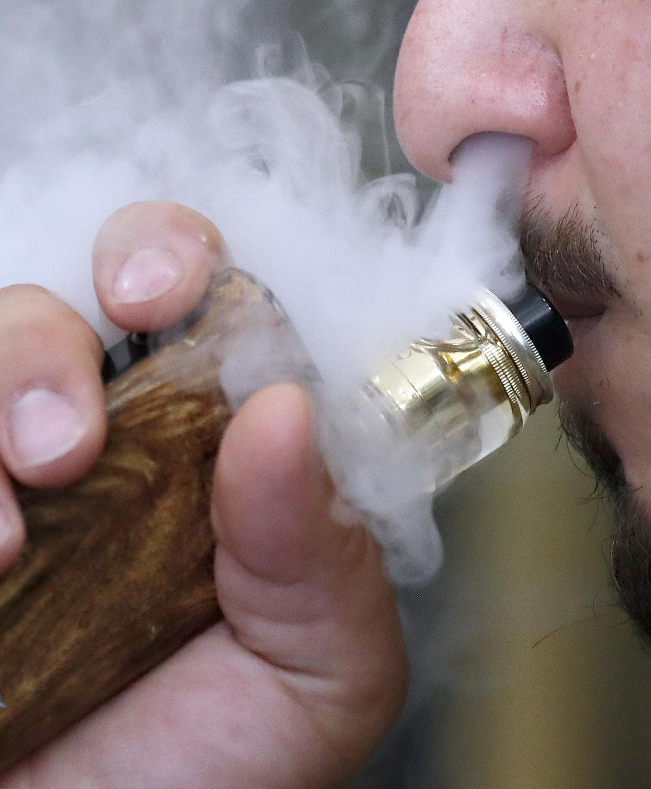FILE - In this Friday, Aug. 17, 2018 file photo, a man breathes vapes from an e-cigarette at a vape shop in London. While the U.S. scrambles to crack down on vaping, Britain has embraced electronic cigarettes as a powerful tool to help smokers kick the habit. (AP Photo/Frank Augstein, File)