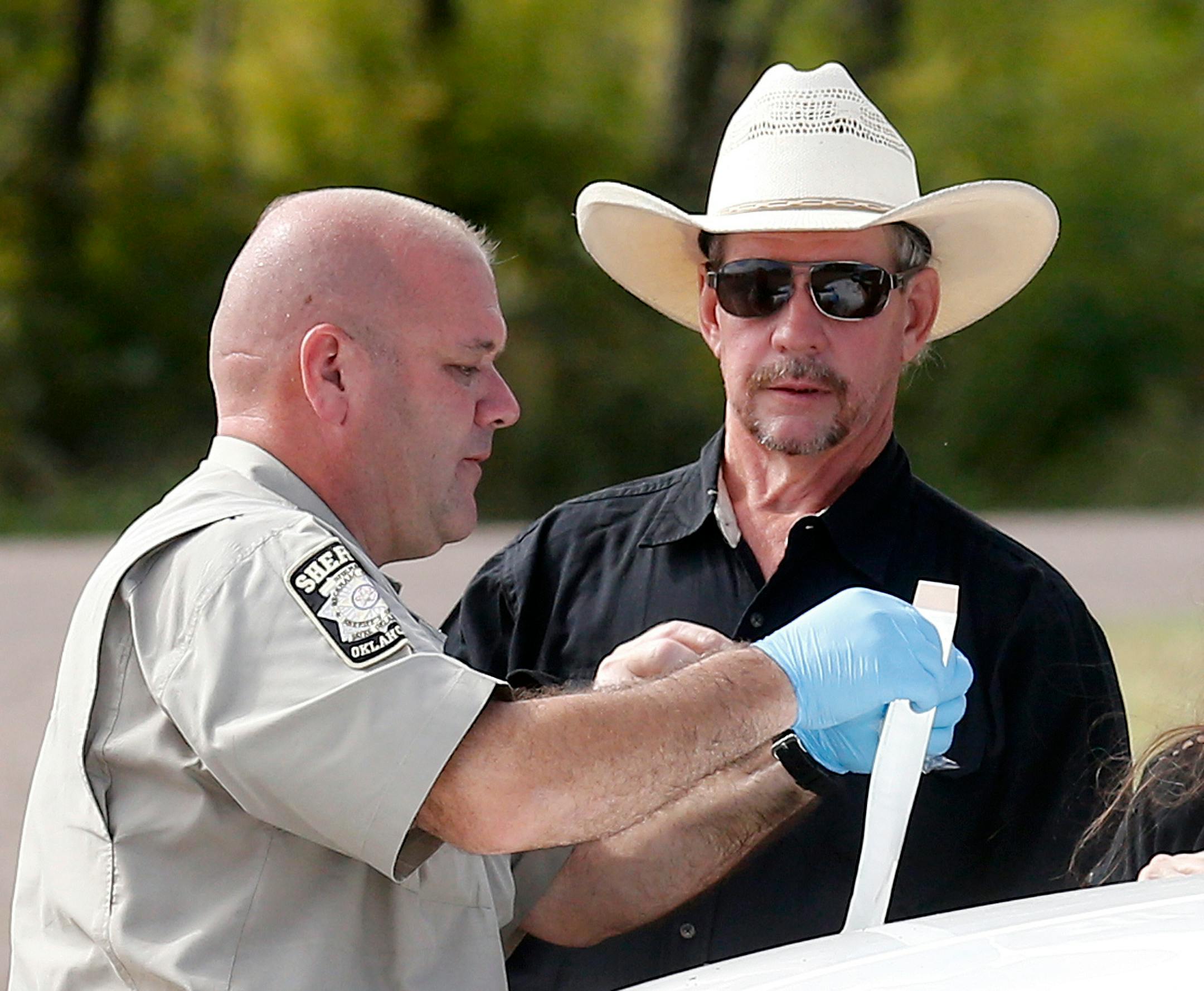 Tim Porter, right, talks with Beckham County Sheriff's Deputy J. Kessel, left, after giving a DNA sample at the scene where two cars were found in Foss Lake, in Foss, Okla., Wednesday, Sept. 18, 2013. Porter says he believes his grandfather's remains may be in one of the cars. The Oklahoma State Medical Examiner's Office says authorities have recovered skeletal remains of multiple bodies in the Oklahoma lake where the cars were recovered.