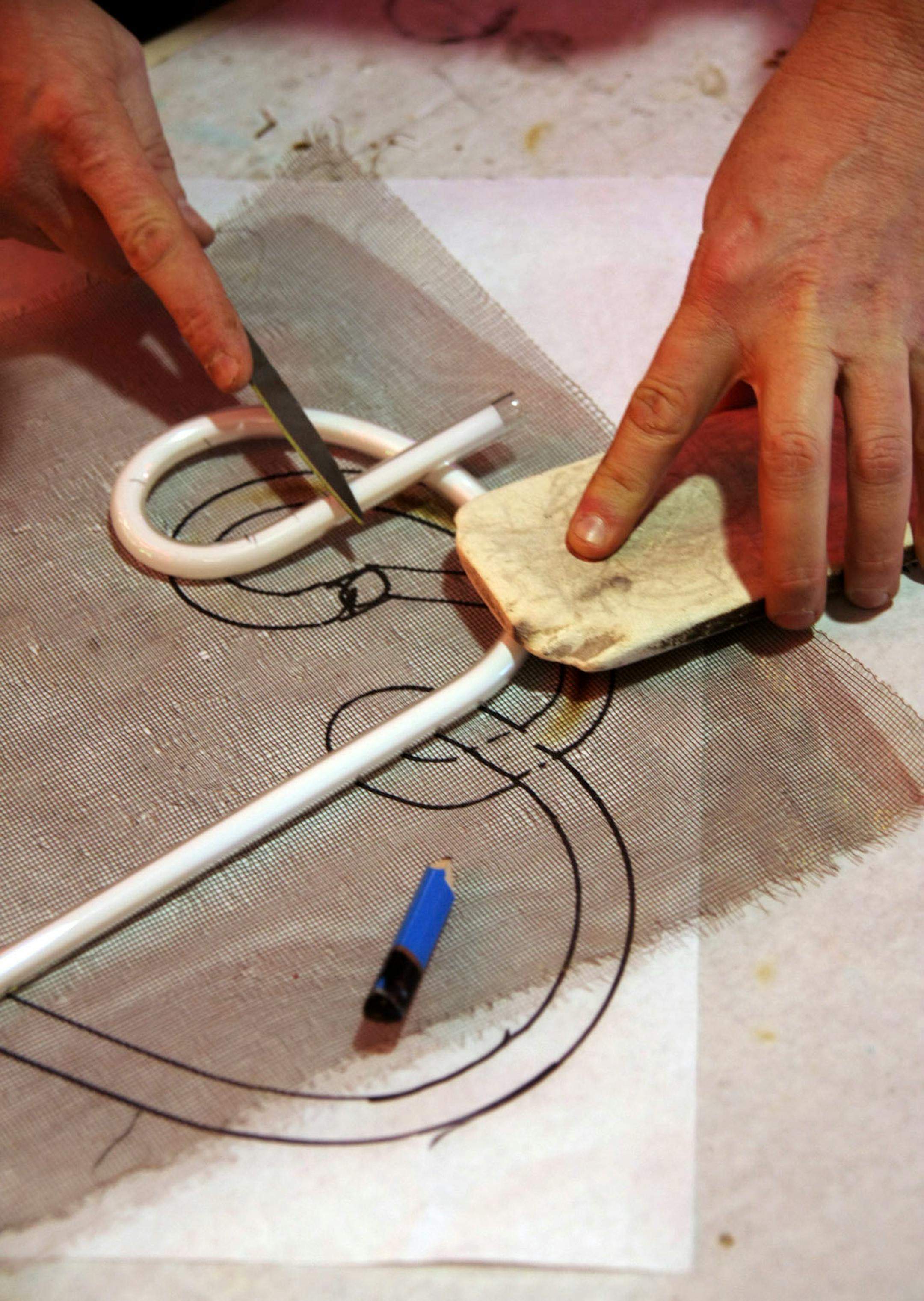 Matt Thompson bends a ( warm) glass tube to a template and cuts of an end,- he is making a piece to repair a sign at a Twin Cities coffee shop.