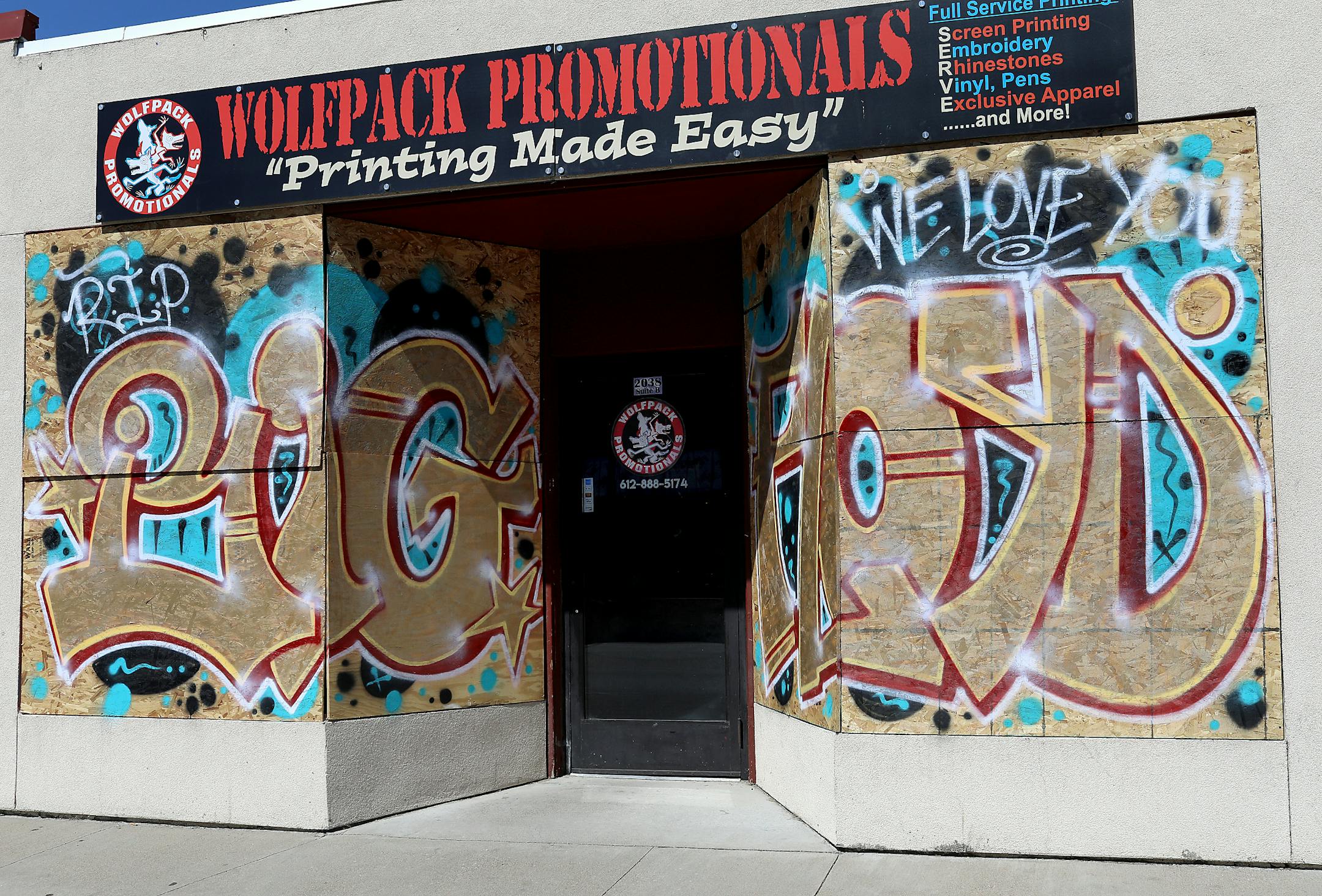 Golden graffiti letters written over boarded-up front windows of Wolfpack Promotionals at 2038 W. Broadway Ave. in north Minneapolis memorialize the death of George Floyd.