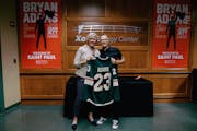 Xcel Energy Center's Kelly McGrath presents rock star Bryan Adams with a Minnesota Wild jersey on July 3, 2023 as they stand backstage in front of con