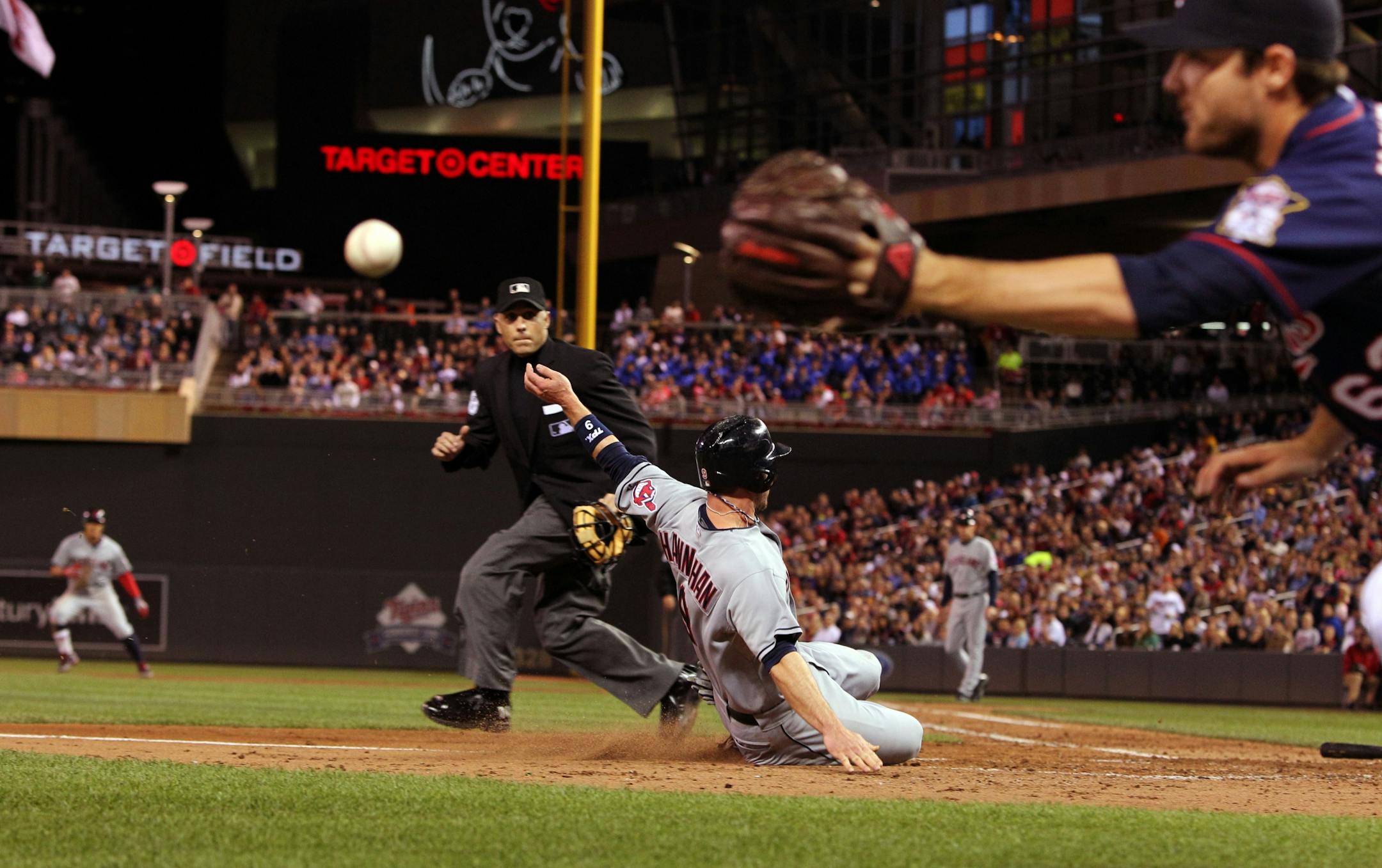 Cleveland Indians' Jack Hannahan (9) slides home safely on teammate Shin-Soo Choo's RBI-single as Minnesota Twins starting pitcher Liam Hendriks, right, chases down the throw to home plate during the fifth inning of a baseball game on Friday, Sept. 7, 2012, in Minneapolis.Home plate umpire Dan Iassogna watches the play.