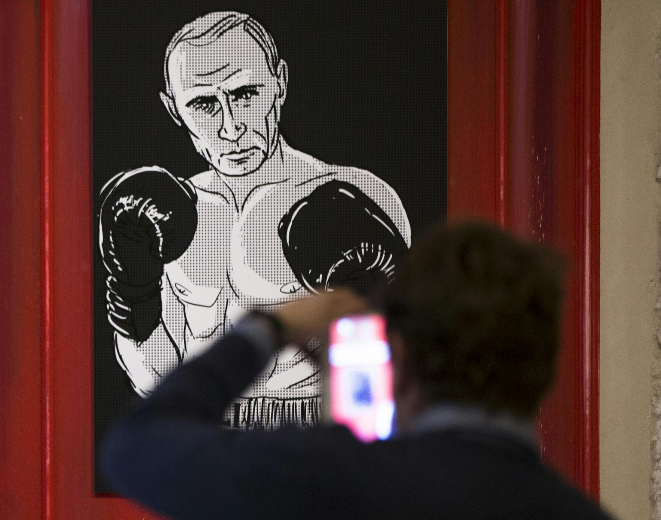 A man takes a picture of an artwork depicting Russian President Vladimir Putin as boxing legend Muhammad Ali during the "Putin Universe" exhibition in Moscow, Russia, Wednesday, Oct. 7, 2015. Artists have drawn the Russian president using 30 heroic themes originating from different countries and world epochs at a two-day exhibition in Moscow. Russian President Vladimir Putin celebrates his 63rd birthday on Wednesday.
