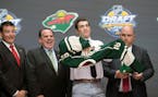 Luke Kunin, second from right, puts on his sweater as he stands with members of the Wild management team at the NHL draft in Buffalo, N.Y., Friday Jun