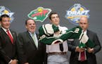 Luke Kunin, second from right, puts on his sweater as he stands with members of the Wild management team at the NHL draft in Buffalo, N.Y., Friday Jun