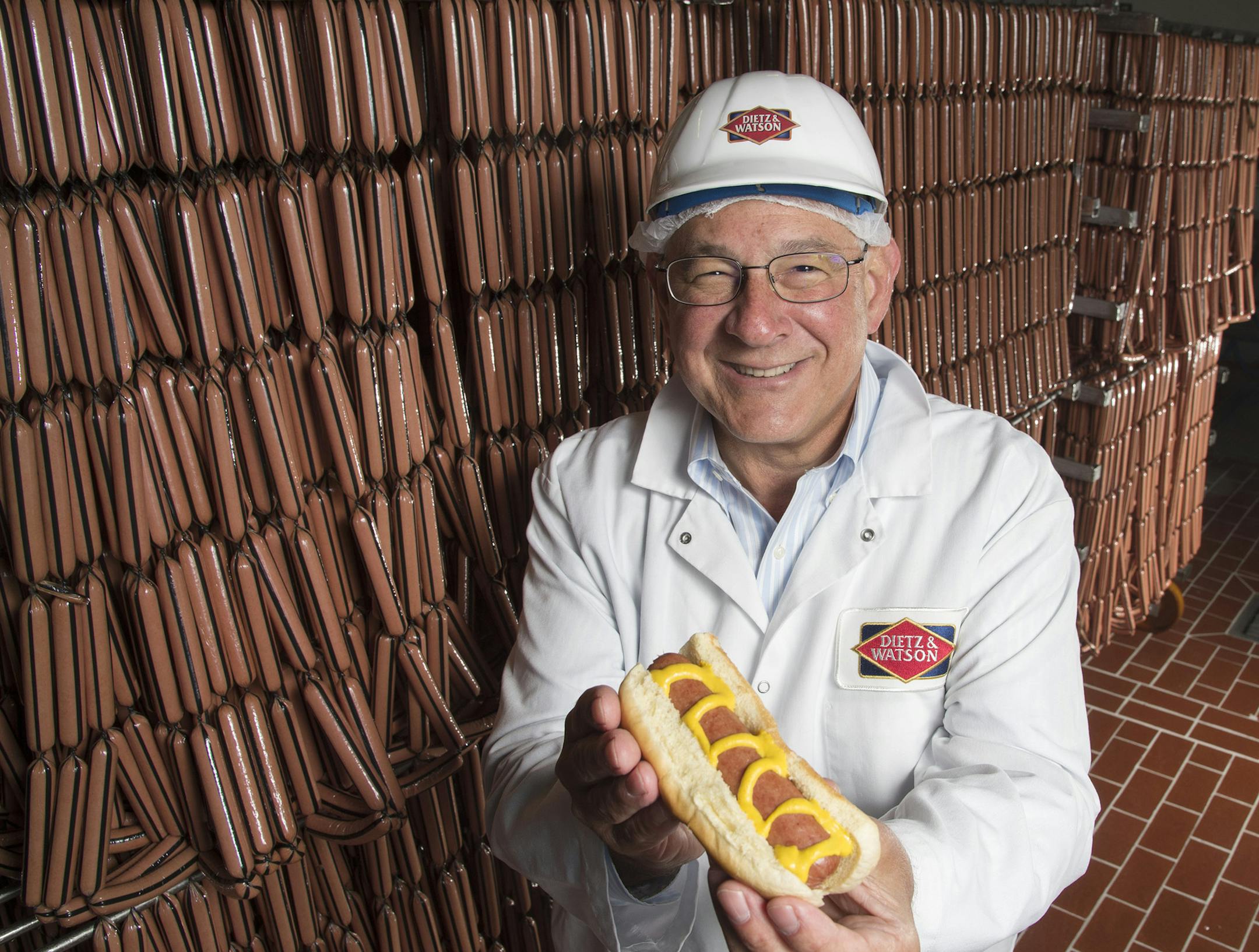 Louis Eni, CEO of Dietz & Watson, displays a cooked hot dog by racks of hot dogs wating to be packaged. (Clem Murray/Philadelphia Inquirer/TNS)