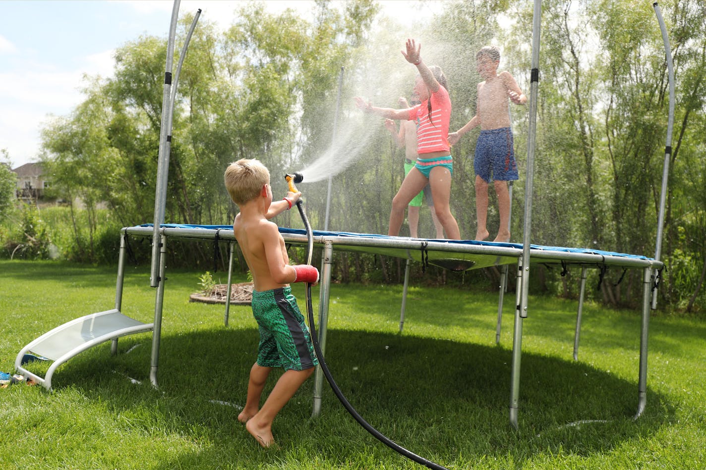 Rusty Golaski, center, 5, sprayed his siblings with a hose as they spent the afternoon playing with their friends on the family's trampoline, despite Rusty's broken arm from a recent fall off of it.