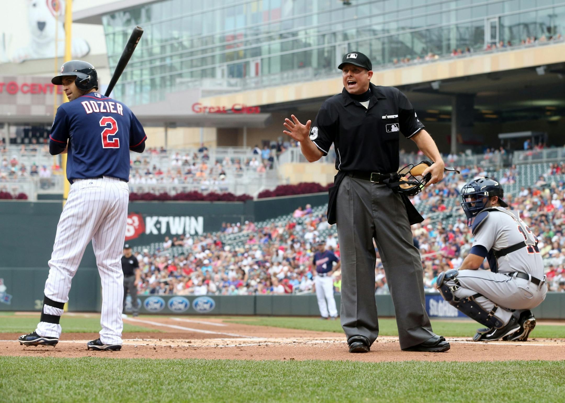 Minnesota Twins batter Brian Dozier, left, looks to the Detroit Tigers dugout as plate umpire Hal Gibson warns the Tiger bench after they complained about Gibson's calls in the first inning of a baseball game, Saturday, Aug. 23, 2014, in Minneapolis. At right is Tigers catcher Alex Avila.
