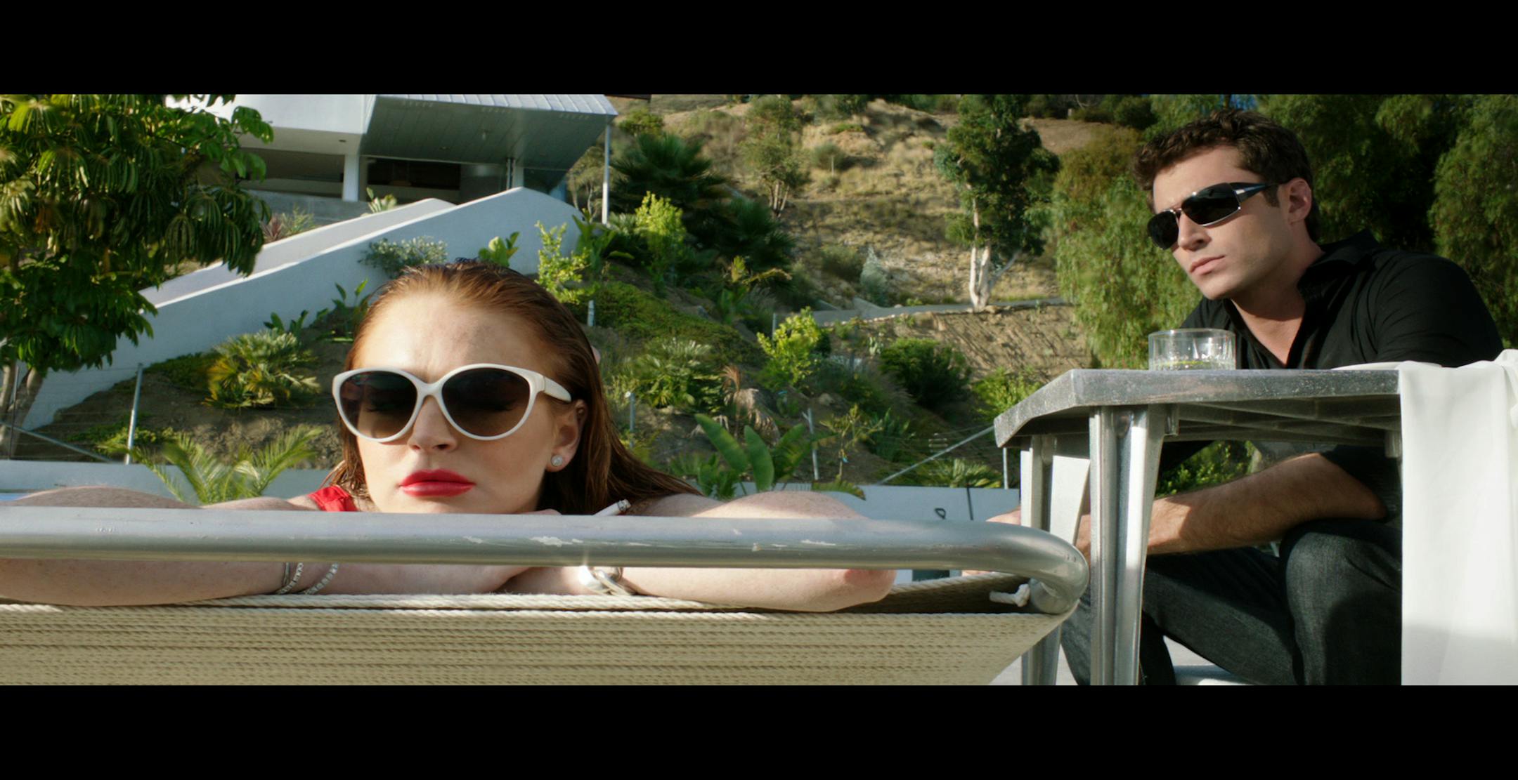 Tara (Lindsay Lohan) lounges poolside with Christian (James Deen) in a scene from Paul Schrader's "The Canyons"