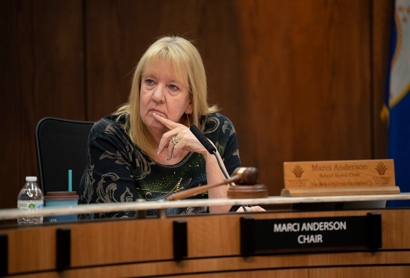 A woman sits at a dais in front of a microphone