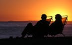 A couple sitting on a California beach at sunset. istock