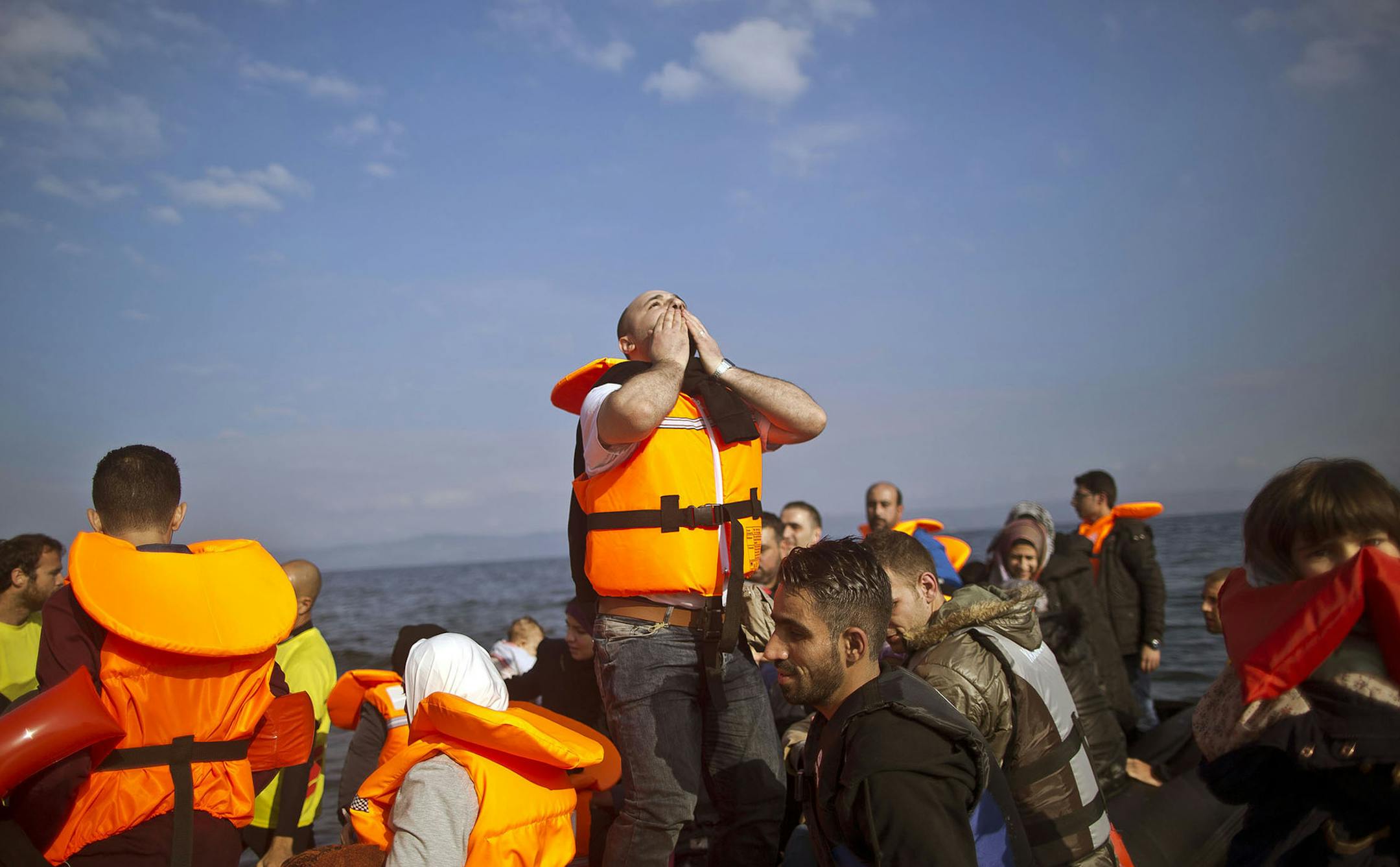 FILE - In this Saturday, Oct. 3, 2015 file photo, Syrian refugee Mahmoud Naoura, 30, center, chants "Thanks God we are safe,"while standing on a dinghy arriving from the Turkish coast to the northeastern Greek island of Lesbos. Bold ideas for helping Syrian refugees and their overburdened Middle Eastern host countries are gaining traction among international donors who were shocked into action by this year's migration of hundreds of thousands of desperate Syrians to Europe. (AP Photo/Muhammed Mu