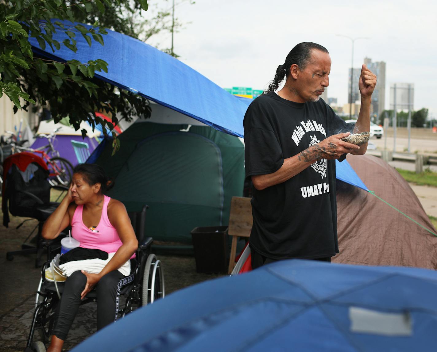 Yvonne, 32, sits in the makeshift camp just off of Hiawatha and Cedar Avenues as James Cross, founder of Natives Against Heroin, burns sage and prays. Later he walked along the encampment to smudge the people and their tents in an act of purification Tuesday, Aug. 7, 2018, in Minneapolis, MN. Yvonne said she moved to the camp about a month ago and says she feels safe at the encampment because she is surrounded by people she knows.