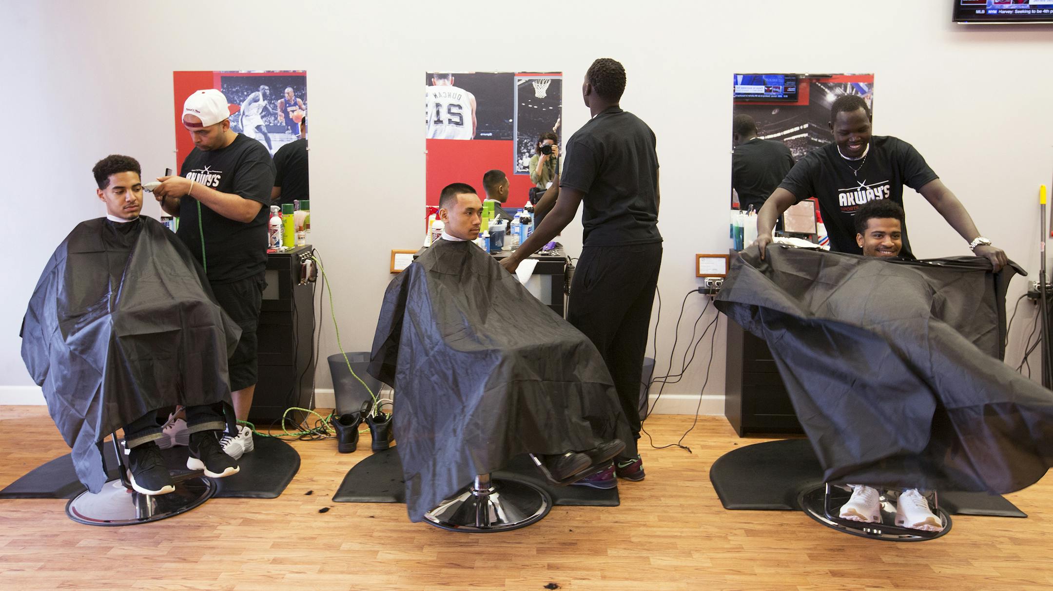 Akeem Akway, right, sits Devan Madison in his chair to cut his hair on opening day of Akway's new business Akway's Sports Barbershop in Spring Lake Park on Friday, May 8, 2015. LEILA NAVIDI leila.navidi@startribune.com / BACKGROUND INFORMATION: Akeem Akway, a former Fridley basketball player, used to cut his teammates' hair in the locker room. From left is Justin Mbanefo, barber Anthony Fitzpatrick, Anthony Keomany and barber Omot Okwan.