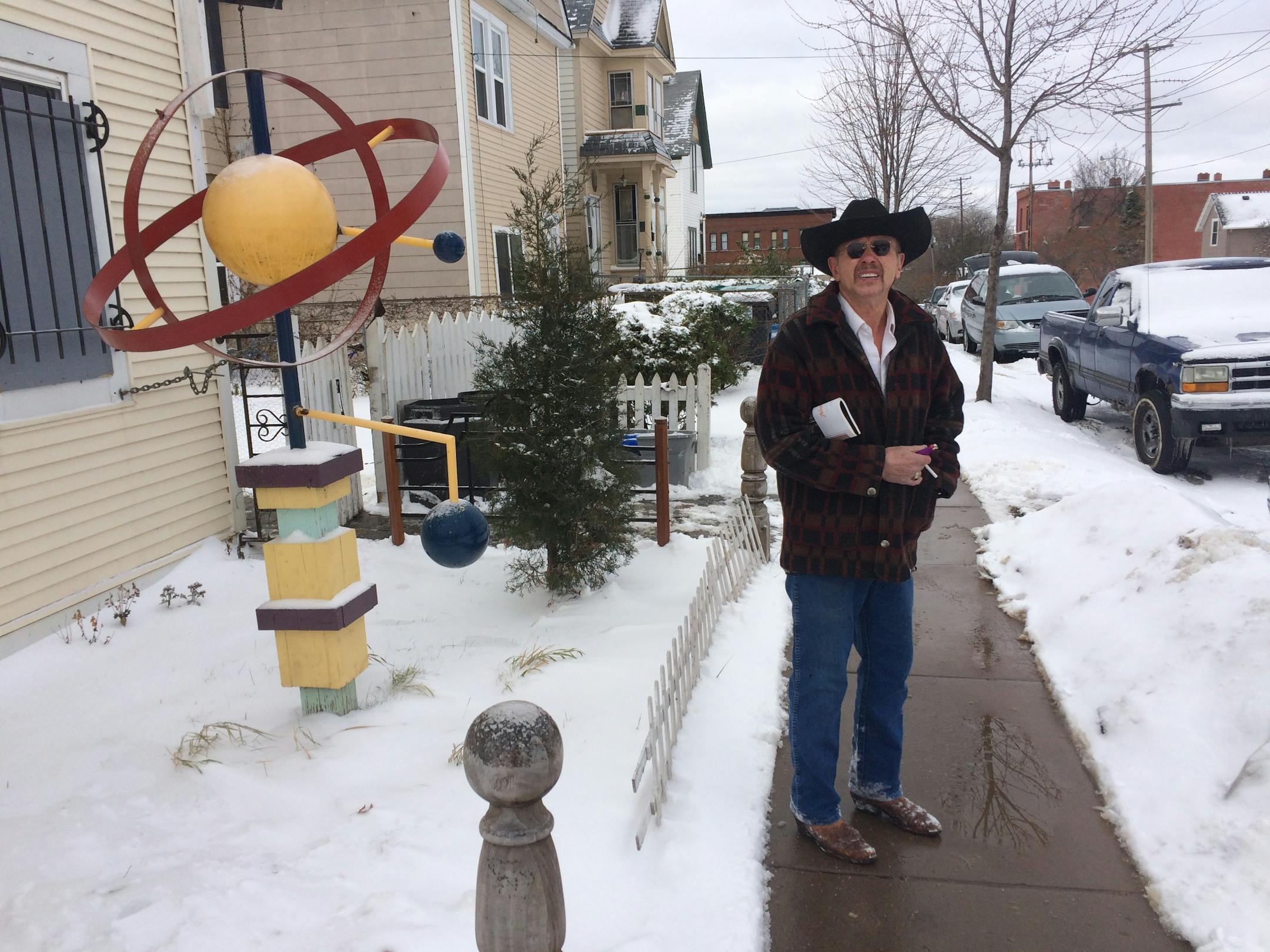 Arjo Adams stands in front of his house, with one of his yard sculptures. He has to use a back door, because the city boarded the front door when it declared the house vacant.