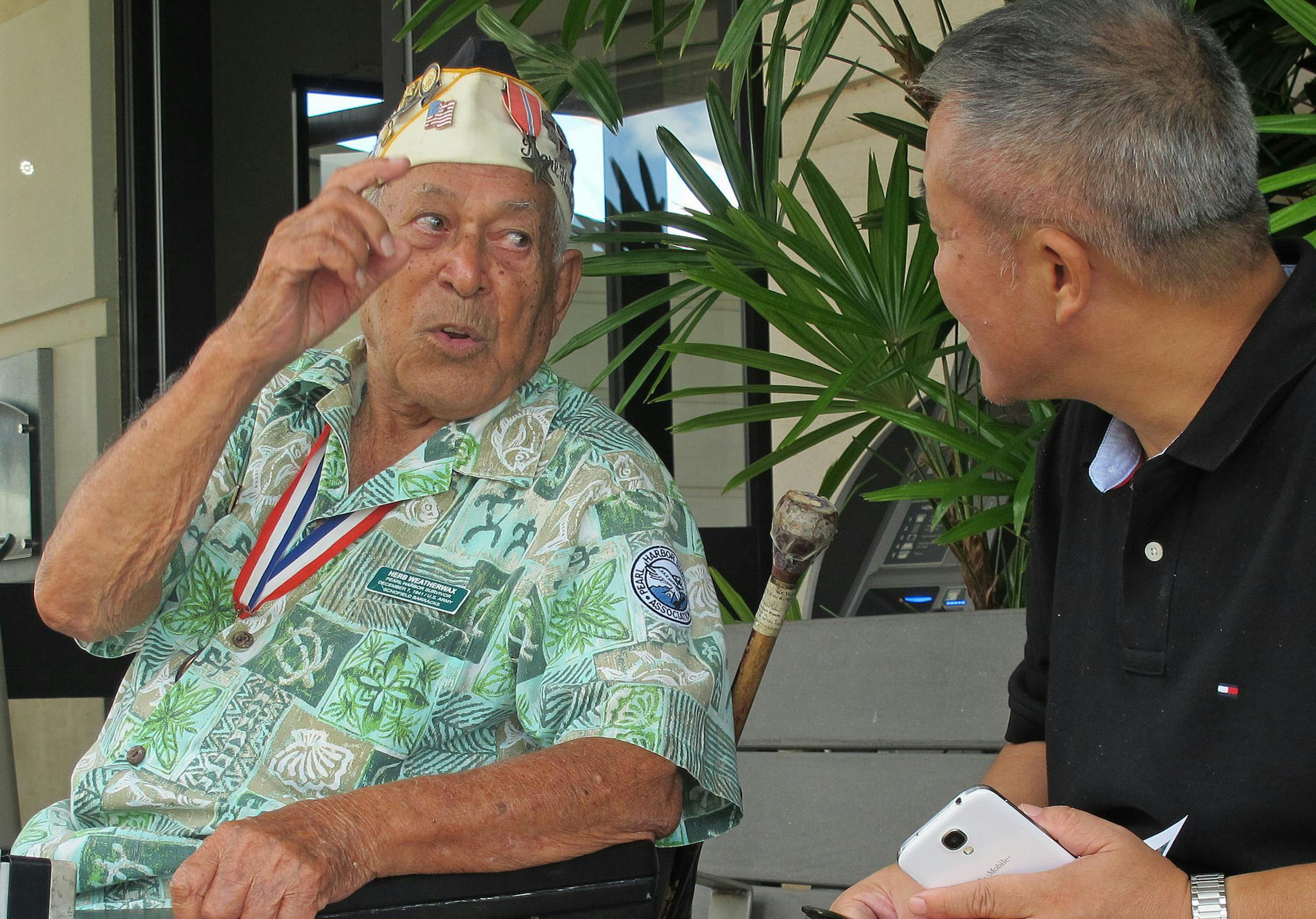 In this photo taken Nov. 22, 2013, Herb Weatherwax, left, talks to a visitor in Pearl Harbor, Hawaii. The 96-year-old retired electrician is one of four Pearl Harbor survivors who volunteers to greet people at the historic site. On Saturday is the 72nd anniversary of the 1941 attack by Japan on Pearl Harbor. (AP Photo/Audrey McAvoy)