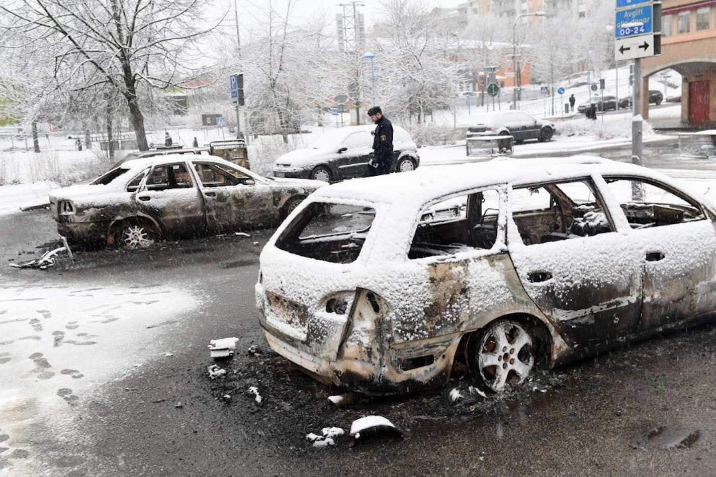 In this picture taken on Monday, Feb. 20, 2017,a policeman investigates a burned out car in the suburb of Rinkeby outside Stockholm. Police in Sweden said Tuesday they were investigating riots that broke out overnight in a predominantly immigrant Stockholm suburb after officers arrested a suspect on drug charges. Spokesman Lars Bystrom said unidentified people, including some wearing masks, threw rocks at police, set cars on fire and looted shops in Rinkeby, north of Stockholm.