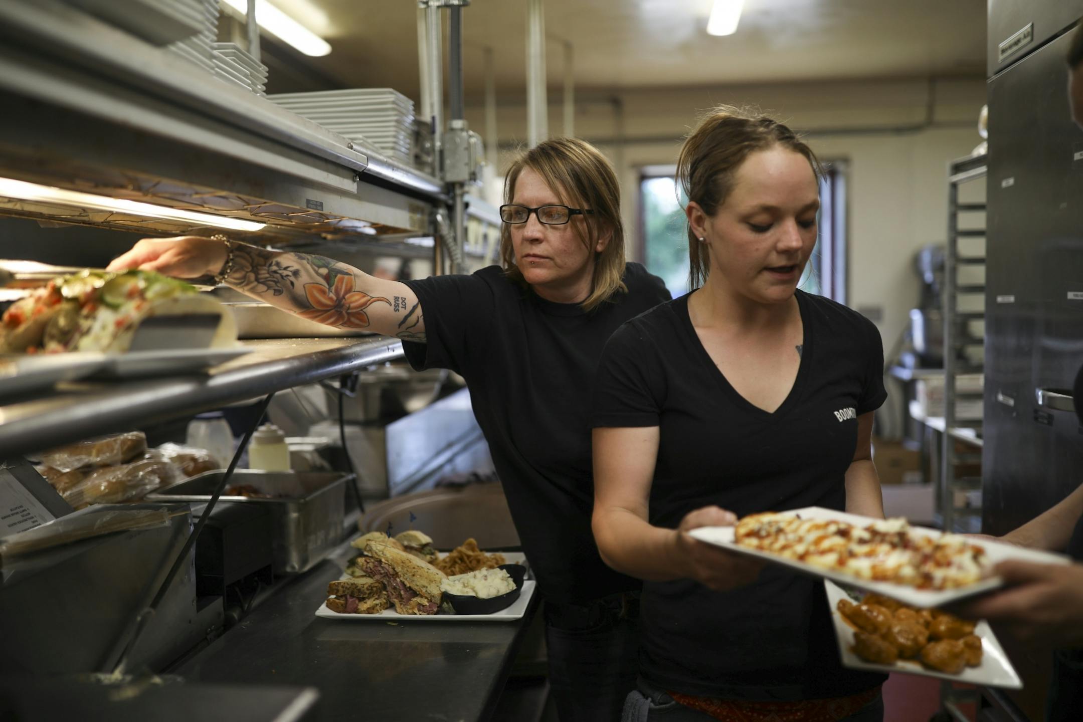Wendi Thompson, left, expedited dinner orders in the kitchen of the BoomTown Brewery & Woodfire Grill during the evening rush Wednesday. At right server Sam Koskela handed off plates to a helper before heading out of the kitchen with the food.