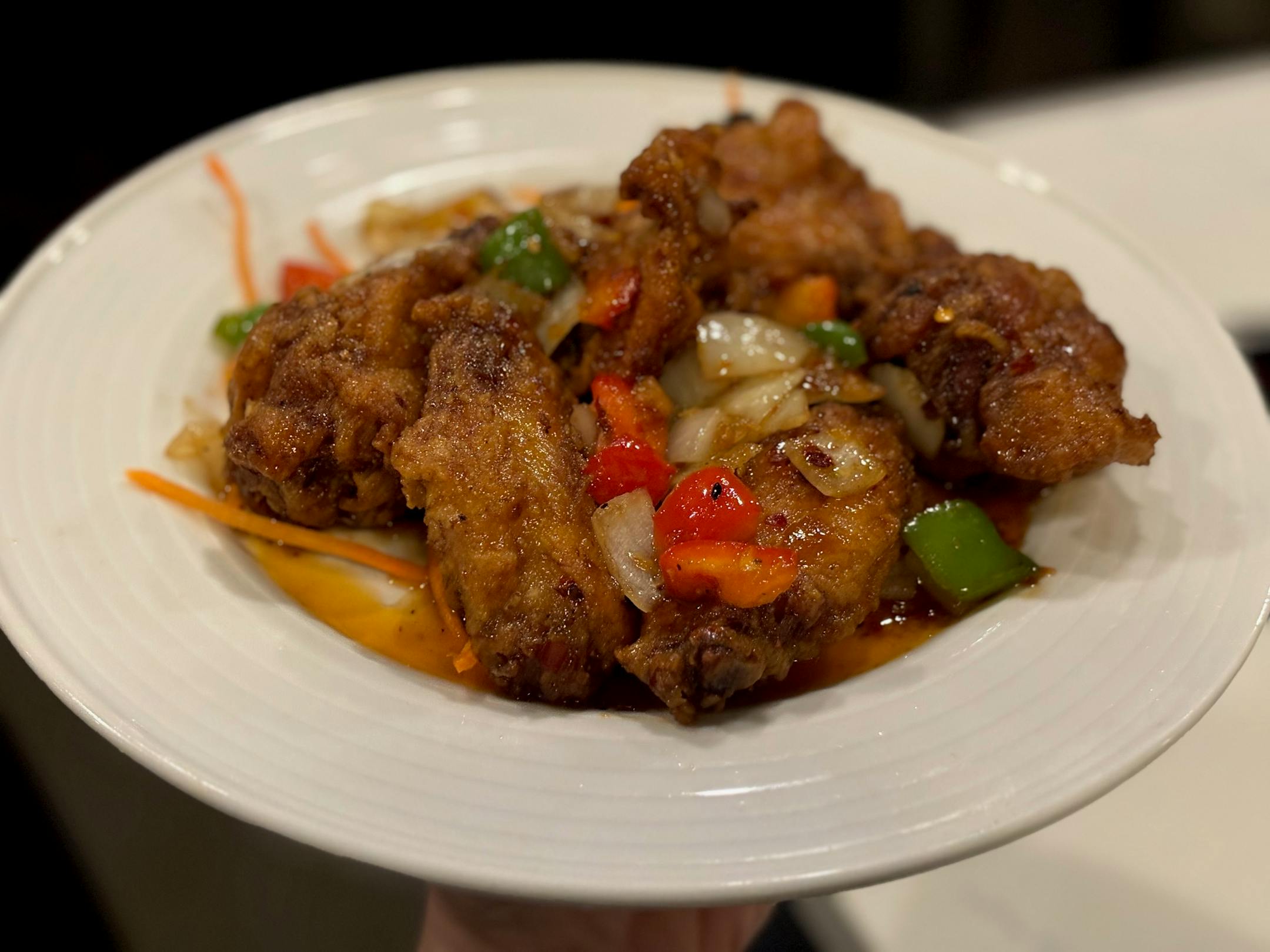 A plate of saucy, battered wings is garnished with bell peppers and onions.
