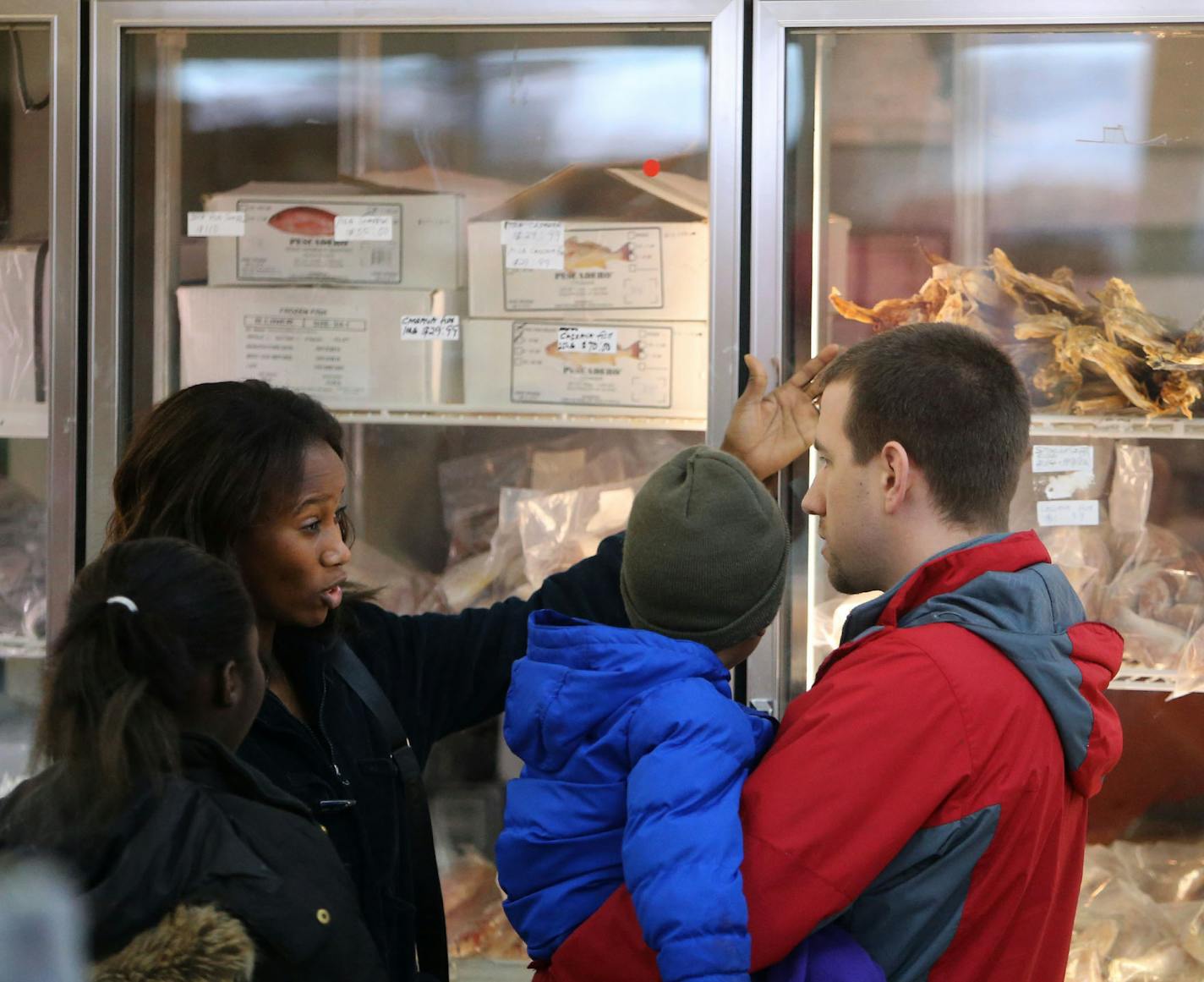 David Bell, right, of Brooklyn Park, holds his son Kirk, 3, while talking to his wife Salamatou Issoufou, as their daughter Halimatou, 13, looks on near the frozen seafood, including dried cod, at BCS African Foods Tuesday, Dec. 23, 2014, in Brooklyn Park, MN.