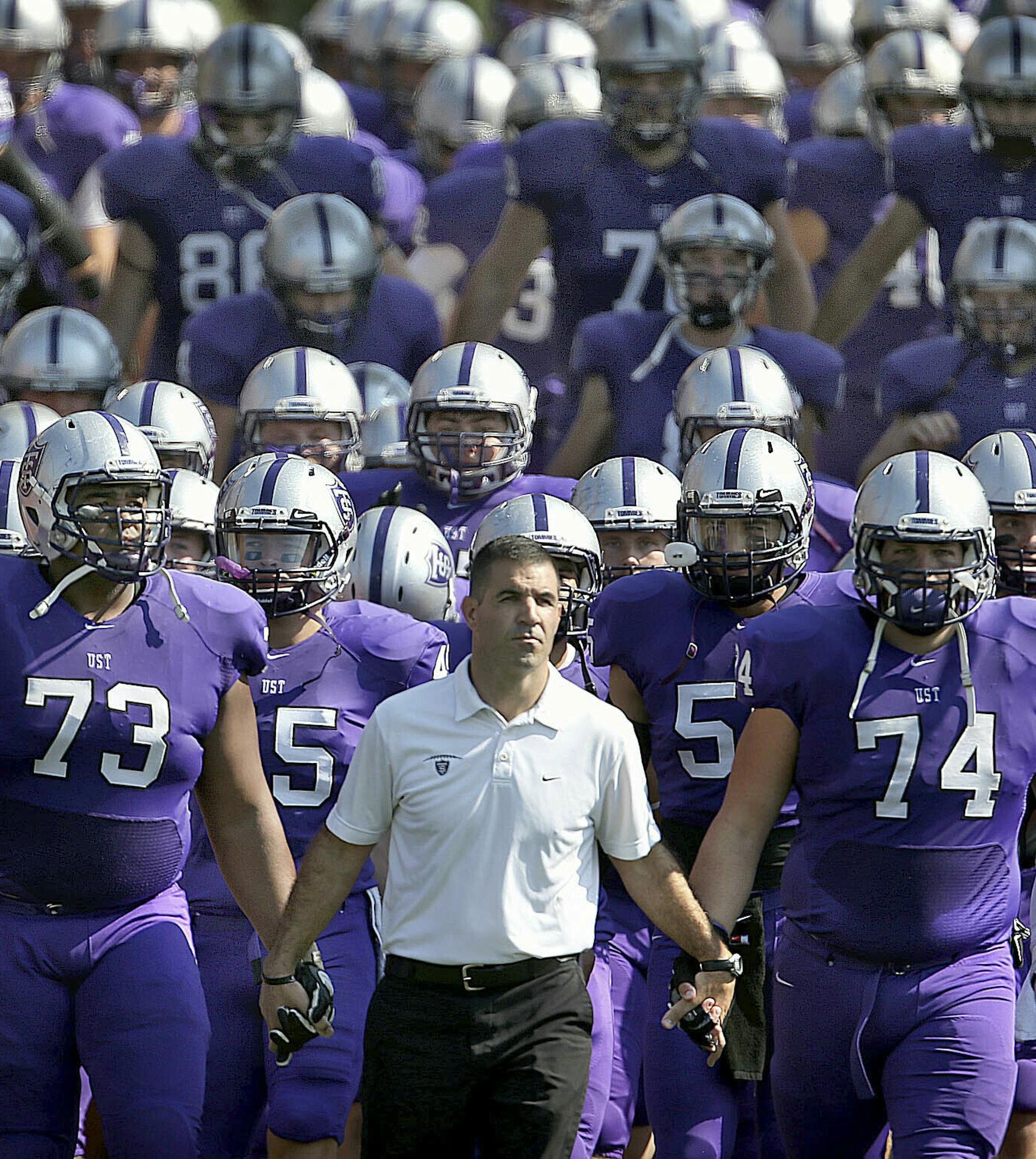FILE - In this Sept. 27, 2014, file photo, St. Thomas coach Glen Caruso leads his team onto the field for a college football game against St. John's, in St. Paul, Minn. The Minnesota Intercollegiate Athletic Conference has decided to oust the NCAA Division III league's largest school, St. Thomas, for competitive purposes. The MIAC announced Wednesday, May 22, 2019, the Tommies will be "involuntarily removed" in two years by the conference they helped found in 1920. (Jim Gehrz/Star Tribune via AP