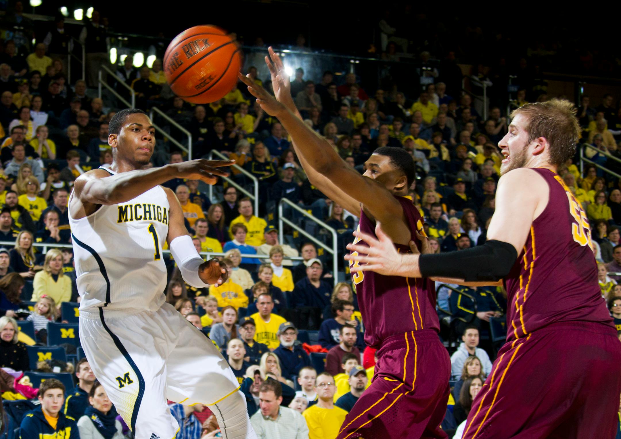 Michigan forward Glenn Robinson III (1) passes the ball past Minnesota forward Charles Buggs, middle, and center Elliott Eliason during the first half of an NCAA college basketball game at Crisler Center in Ann Arbor, Mich., Saturday, March 1, 2014. (AP Photo/Tony Ding)