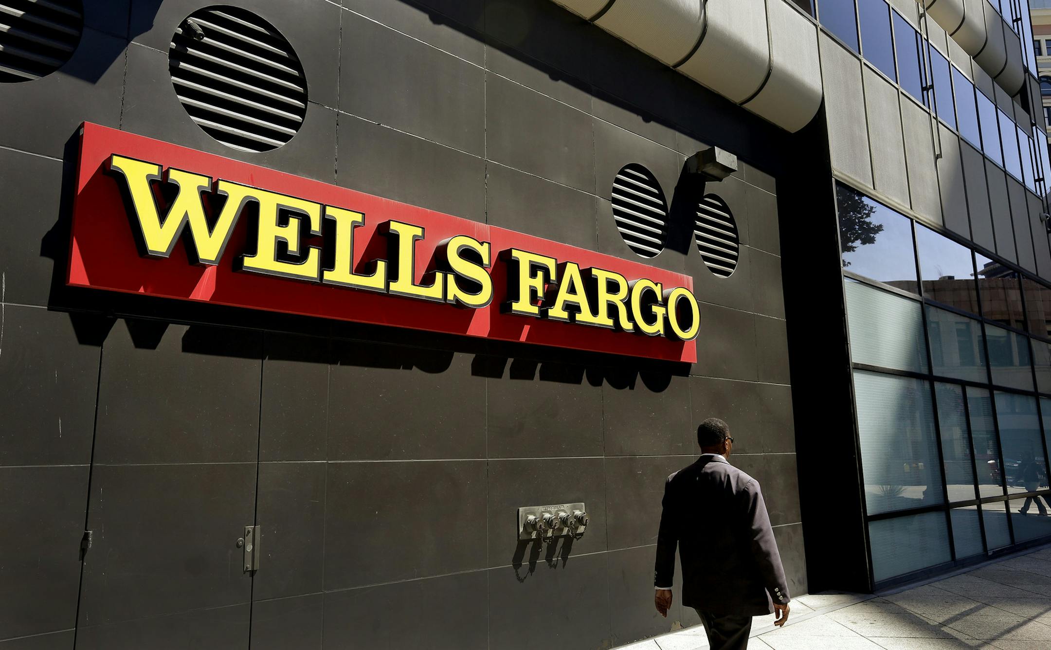In this July 14, 2014, file photo, a man passes by a Wells Fargo bank office in Oakland, Calif.