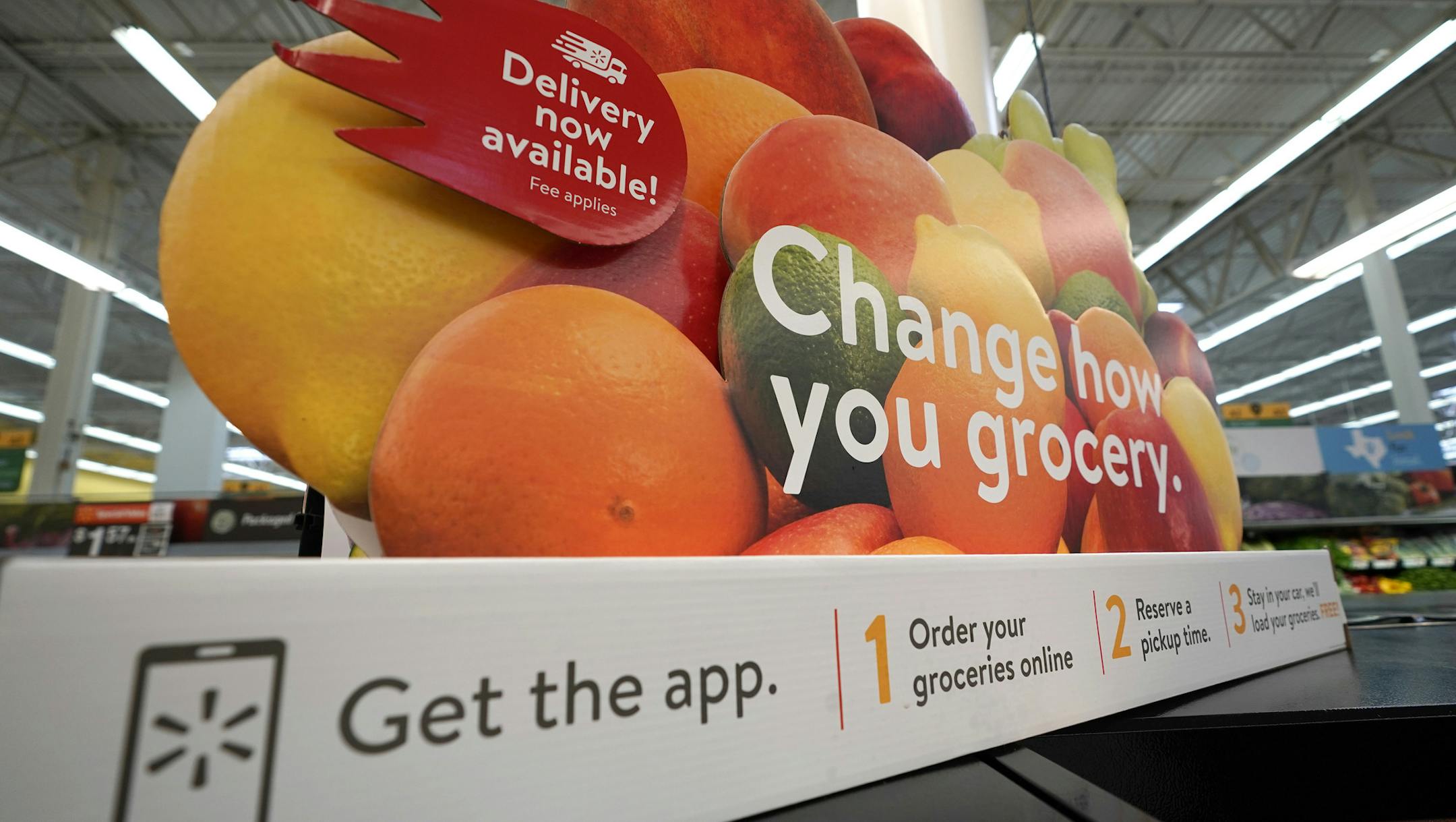 FILE- In this Nov. 9, 2018, file photo a sign promotes online and home delivery of groceries at a Walmart Supercenter in Houston. Grocery delivery services are growing rapidly, but shoppers need to decide if the convenience is worth the higher cost. Big companies like Amazon and Walmart are expanding grocery delivery, as are regional players like FreshDirect. (AP Photo/David J. Phillip, File)
