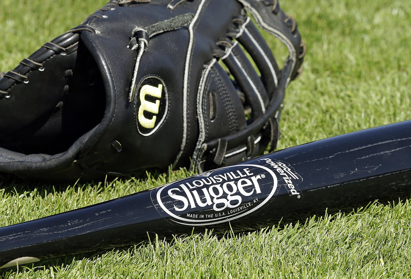 A Wilson baseball glove and a Louisville slugger bat sit on the field prior to a spring training baseball game between the Kansas City Royals and the San Francisco Giants on Monday, March 23, 2015, in Scottsdale, Ariz. Hillerich & Bradsby Co., the company that made bats for a who's who of baseball greats, including Babe Ruth and Ted Williams, announced a deal Monday to sell its Louisville Slugger brand to rival Wilson Sporting Goods Co. for $70 million. (AP Photo/Ben Margot)