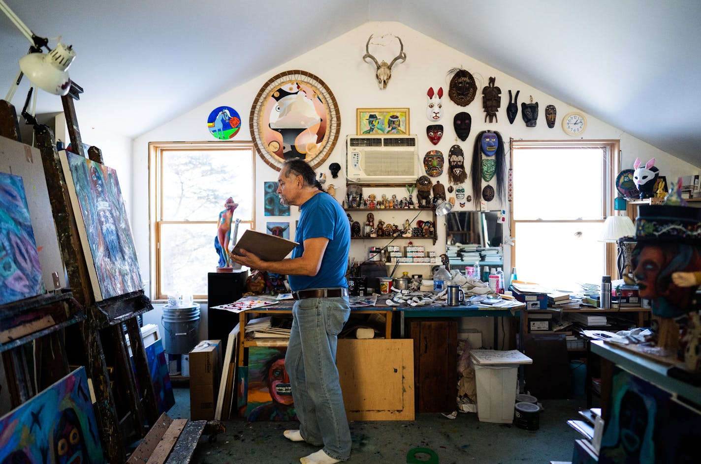 Denomie work surrounded by his own paintings and a vast collection of masks. ] MARK VANCLEAVE ¥ Minnesota artist Jim Denomie works in his Shafer, Minn. studio Friday, Jan. 25, 2019.