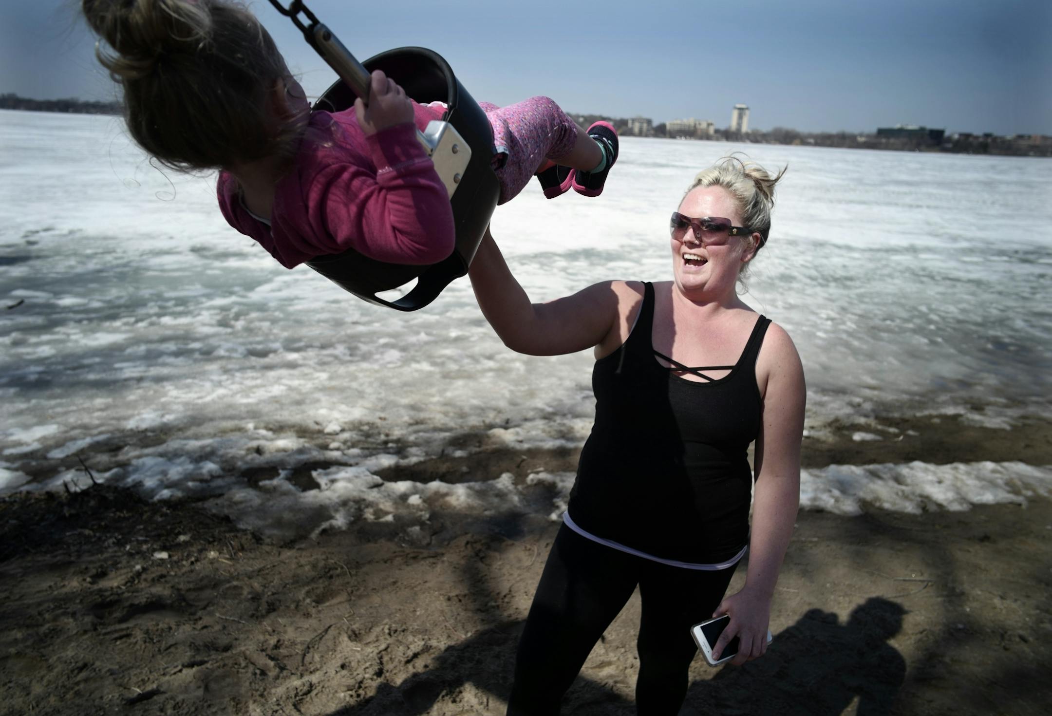On Bde Maka Ska, Kristi Nemcek soaked in the warm weather with daughter Nova, 2.5, on the swings. It is their first at a public playground this spring.