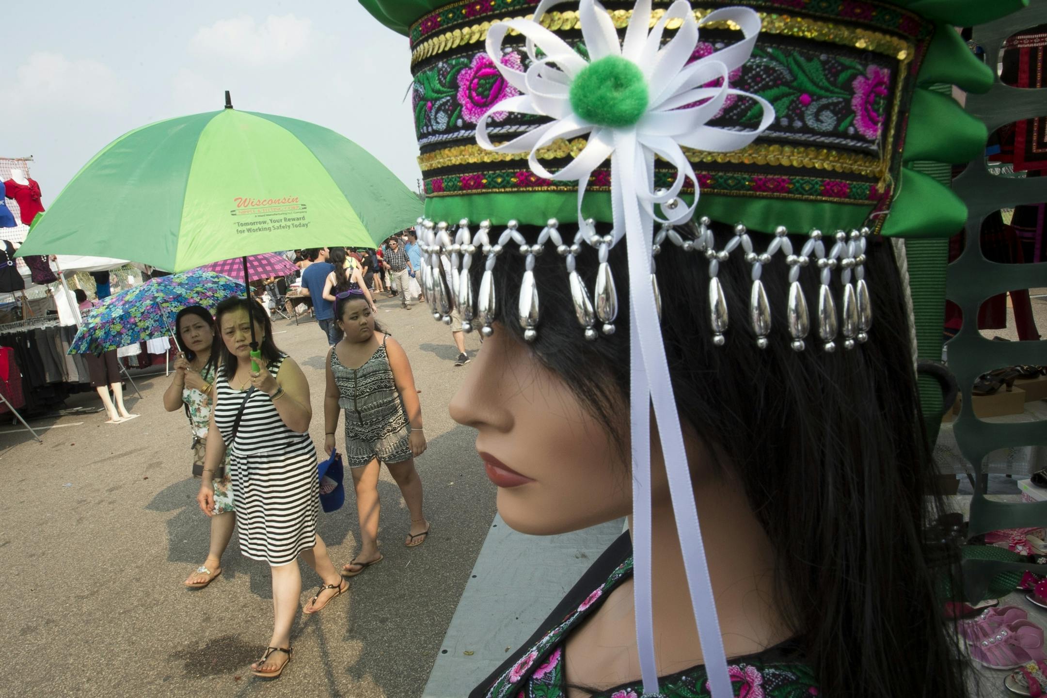 Xee Thao, front, of Milwaukee, walked with her sister, Ka Thao, left and niece, Katrina Lee, past a mannequin donning a traditional Hmong dress on Saturday afternoon in one of the Festival's shopping strips.