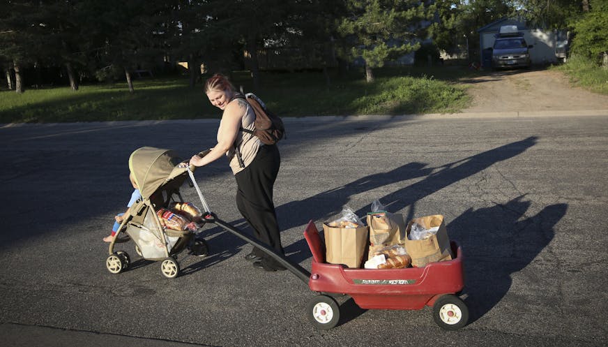 Tara Nordgren walked home with her son Allan in a stroller and a wagon she had attached by a belt to the handle of the stroller to bring home the groceries she had got at the Anoka County Brotherhood Council food shelf in Anoka, Minn., on Thursday, June 18, 2015. Nordgren works at Burger King but as a single mom needs help with groceries since her food stamps were cut back. She doesn't own a car. ] RENEE JONES SCHNEIDER &#x2022; reneejones@startribune.com