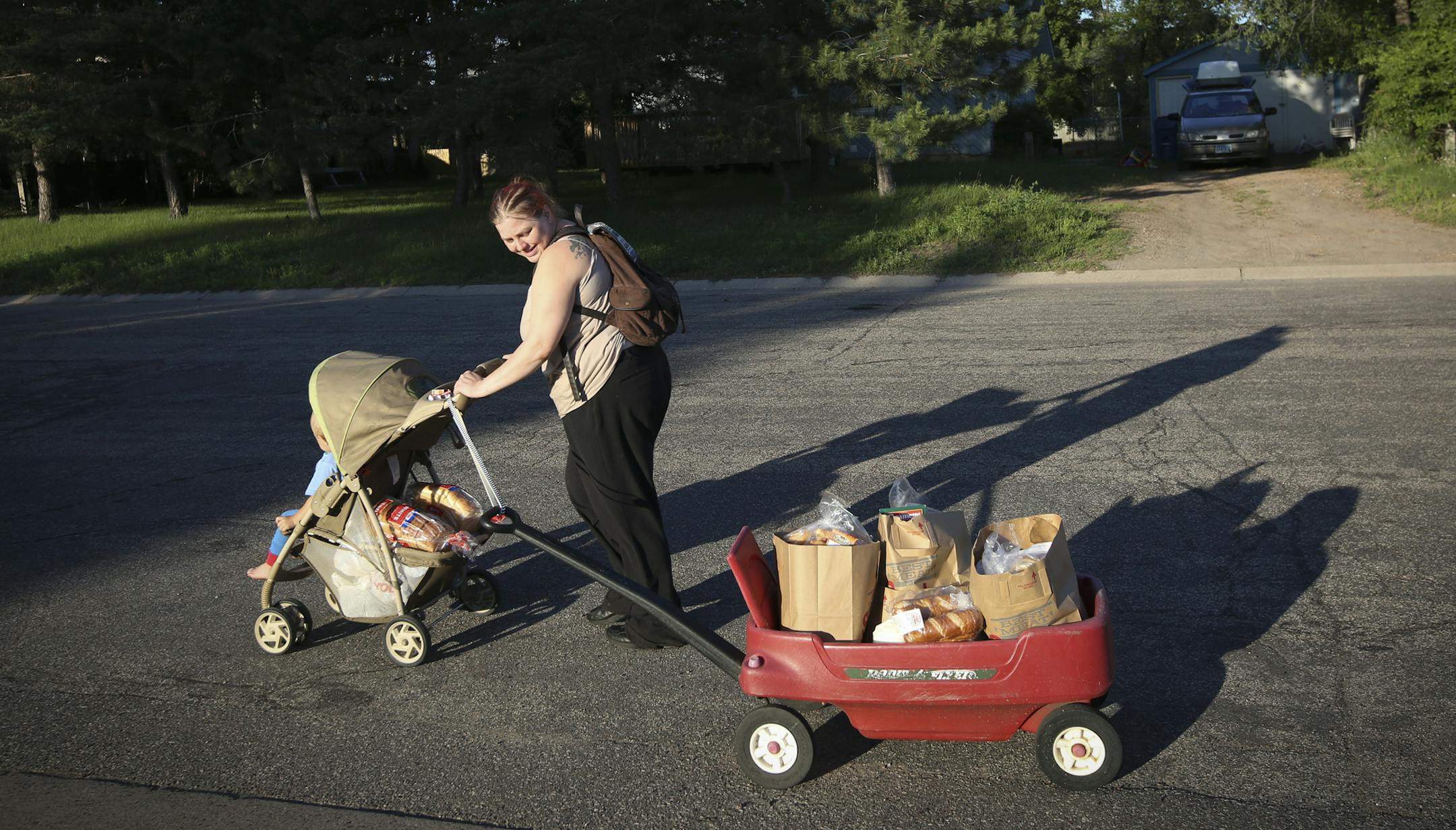 Tara Nordgren walked home with her son Allan in a stroller and a wagon she had attached by a belt to the handle of the stroller to bring home the groceries she had got at the Anoka County Brotherhood Council food shelf in Anoka, Minn., on Thursday, June 18, 2015. Nordgren works at Burger King but as a single mom needs help with groceries since her food stamps were cut back. She doesn't own a car. ] RENEE JONES SCHNEIDER &#x2022; reneejones@startribune.com