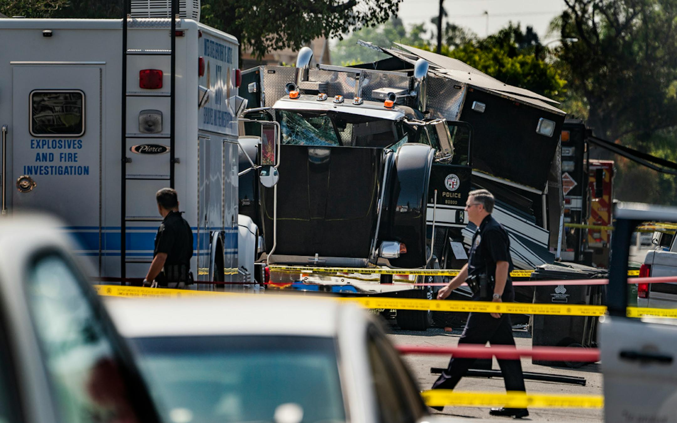 FILE - In this July 1, 2021 file photo Police officers walk past the remains of an armored Los Angeles Police Department tractor-trailer, after illegal fireworks seized at a South Los Angeles home exploded, in South Los Angeles. Los Angeles bomb technicians grossly miscalculated the weight of homemade fireworks last month when they detonated them in a containment chamber, causing a catastrophic explosion that injured 17 people and rocked a neighborhood, the police chief said Monday, July 19, 2021. (AP Photo/Damian Dovarganes,File)