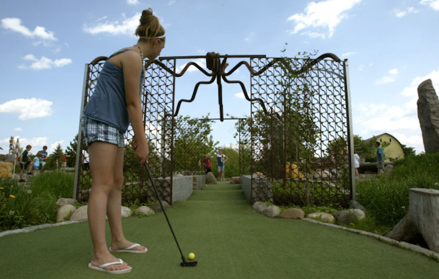 Jenny Graphenteen (13), lines up her putt on the fourth hole called the Arbor Viney. Brendan Dreyer (8) red shirt, and Sydney Dreyer (12) from Minnetrista, MN wait for her at he hole. Bruce Stillman owns Bigstone mini golf and Sculpture gardens is the newest miniature-golf course in Minnetrista. The Big Stone course is built around objects d�art, and really good ones at that.