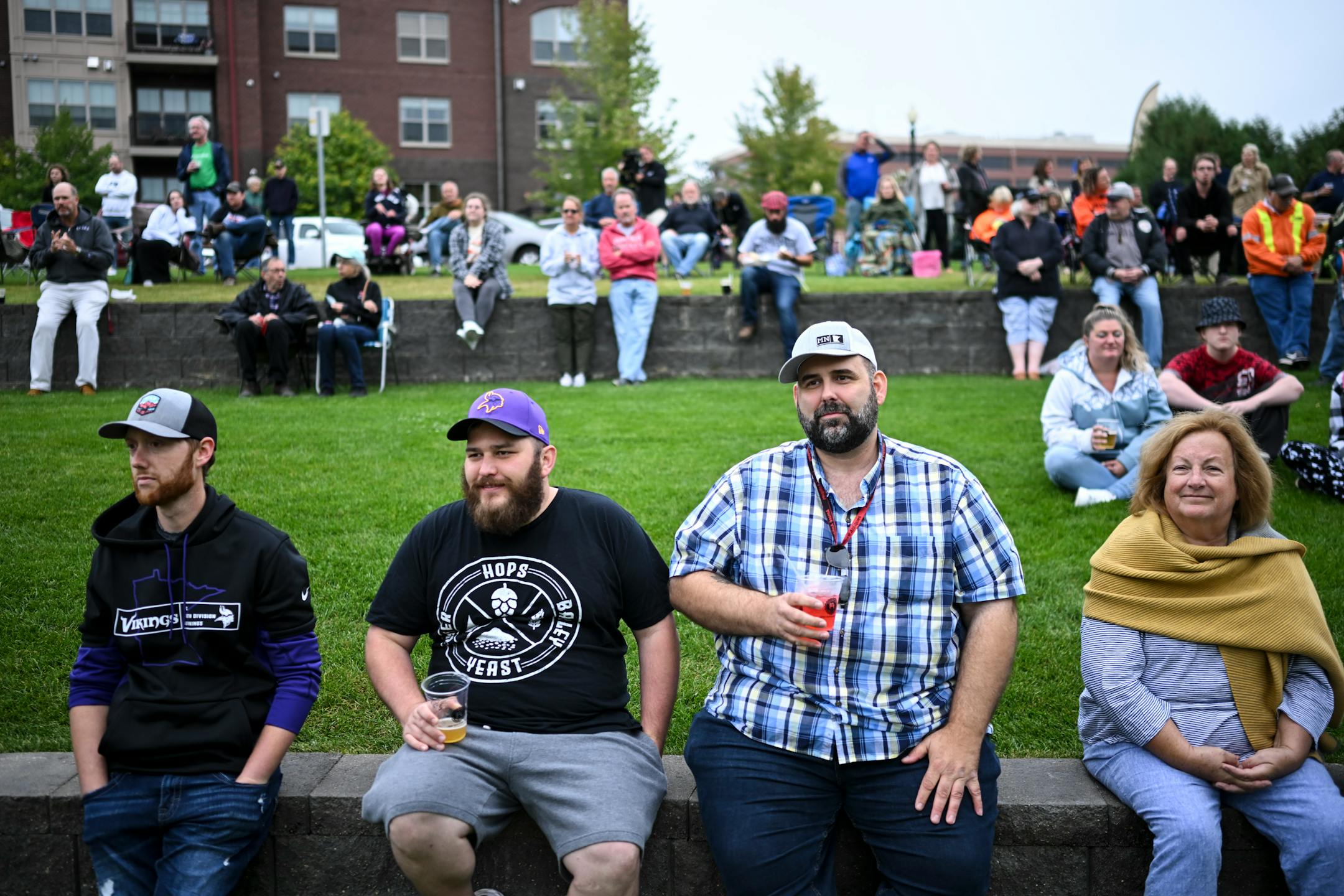 Amore Antiques shop owner Brandon Altenweg, right of center, sits beside friend Shane Eckman, drinks in hand, Wednesday, Sept. 6, 2023 at Riverfront Memorial Park in Anoka, Minn. Starting Wednesday, anybody 21 and older may buy adult beverages from some bars and restaurants in Anoka and consume them as they walk on sidewalks, into shops that allow it, and along the riverfront in the city's historic downtown. The social district will pilot a project as a way to generate activity and bring people together. ] AARON LAVINSKY • aaron.lavinsky@startribune.com