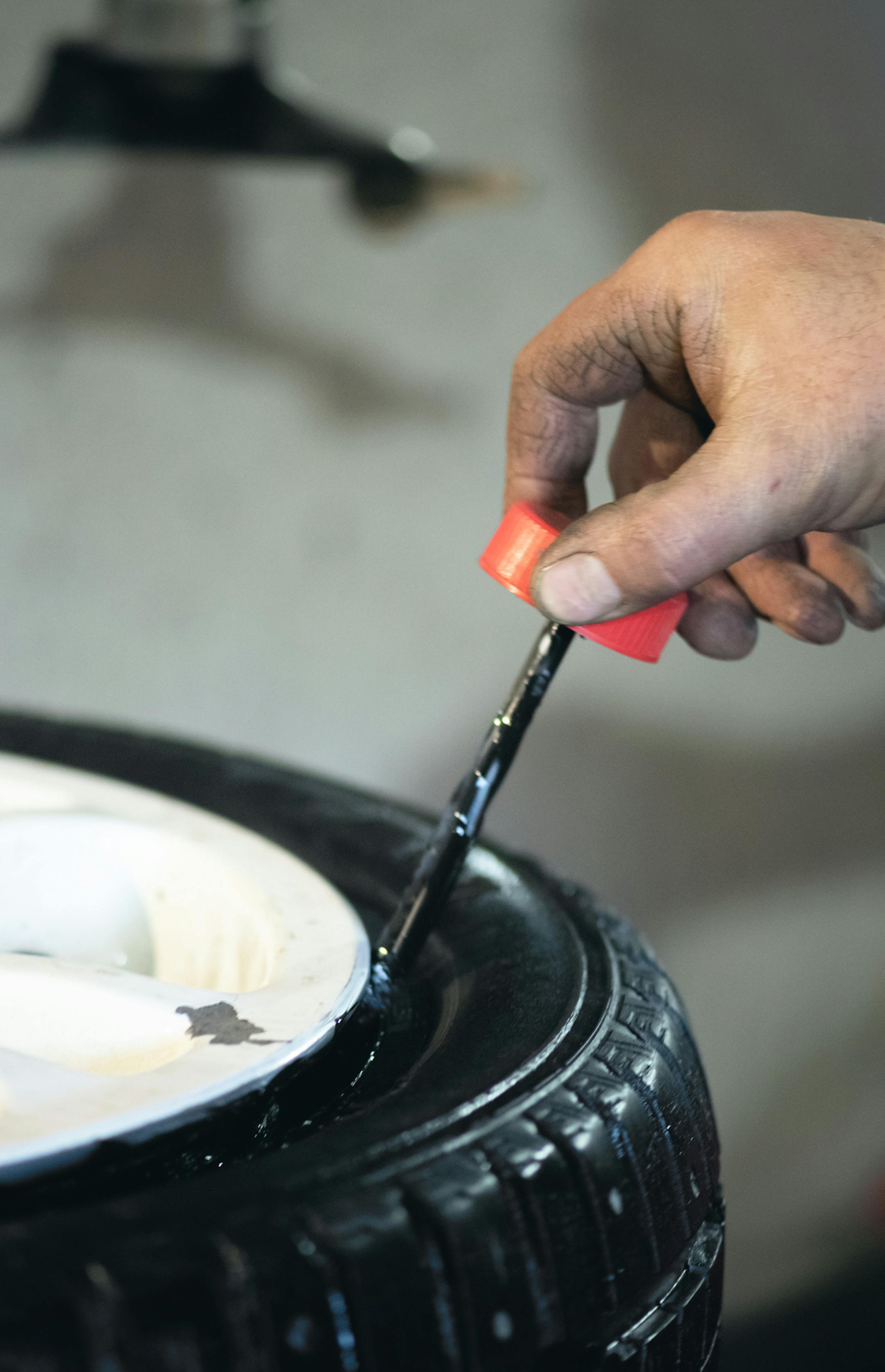 Worker of auto service station is glueing by sealant a wheel rim close up. Defocused image.