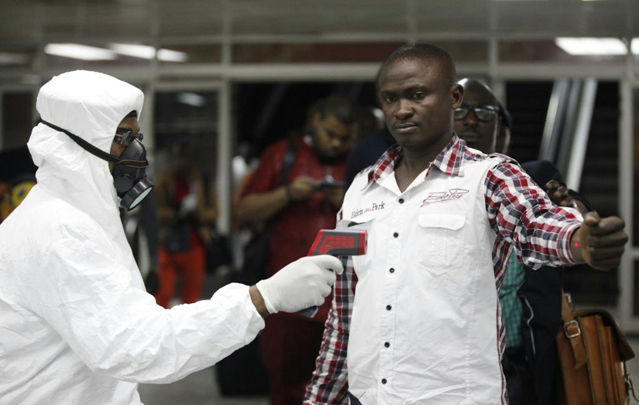 FILE - In this Aug. 6, 2014 file photo, a Nigerian port health official uses a thermometer on a worker at the arrivals hall of Murtala Muhammed International Airport in Lagos, Nigeria. As the Ebola outbreak in West Africa grows, airlines around the globe are closely monitoring the situation but have yet to make any drastic changes. (AP Photo/Sunday Alamba, File)