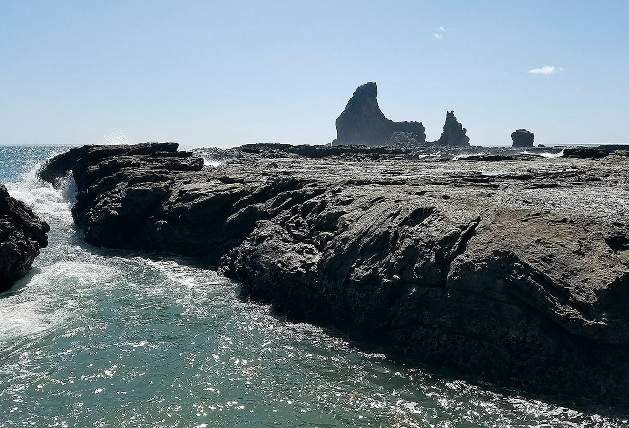 Pacific waves fill a deep trench in the rocks at Playa Maderas, Nicaragua, with a "shark's tooth" promontory in the background.