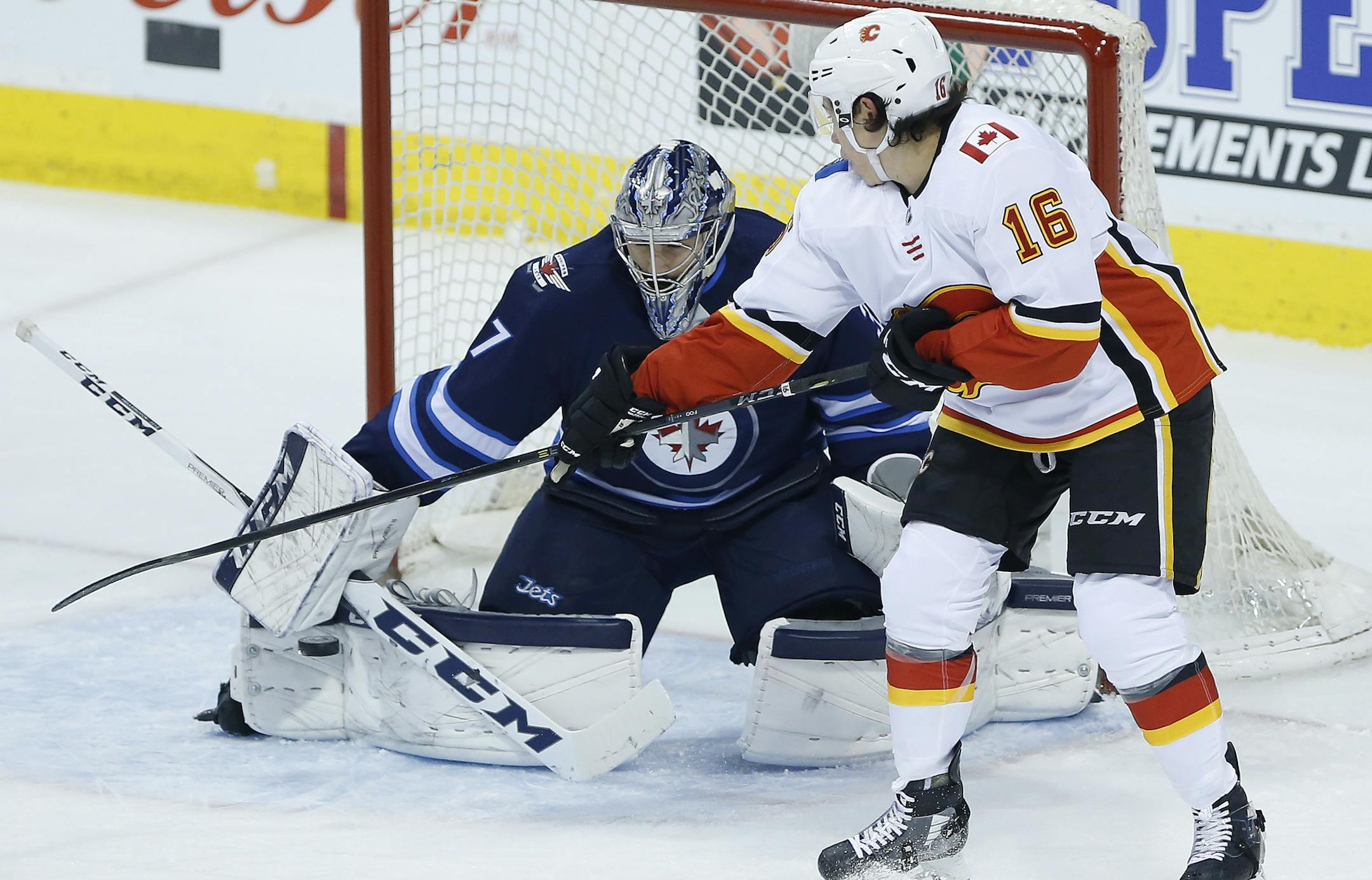 Calgary Flames' Spencer Foo (16) attempts to tip the puck past Winnipeg Jets goaltender Connor Hellebuyck (37) during the first period of an NHL hockey game Thursday, April 5, 2018, in Winnipeg, Manitoba. (John Woods/The Canadian Press via AP)