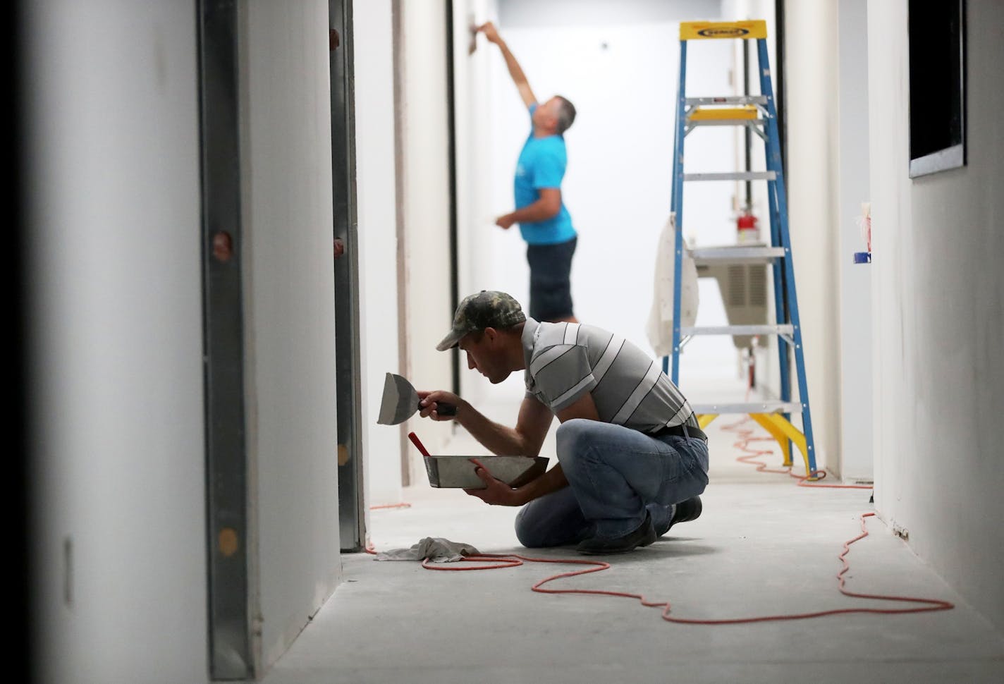 Vasiliy Chobanu, front, and Andrey Gubceai, trowel joint compound onto walls at an office remodel for Adhesive Systems Technology in Brooklyn Center.