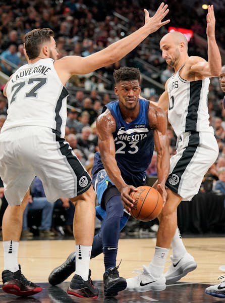 Minnesota Timberwolves' Jimmy Butler (23) looks to pass as he drives between San Antonio Spurs' Joffrey Lauvergne, left, of France, and Manu Ginobili,