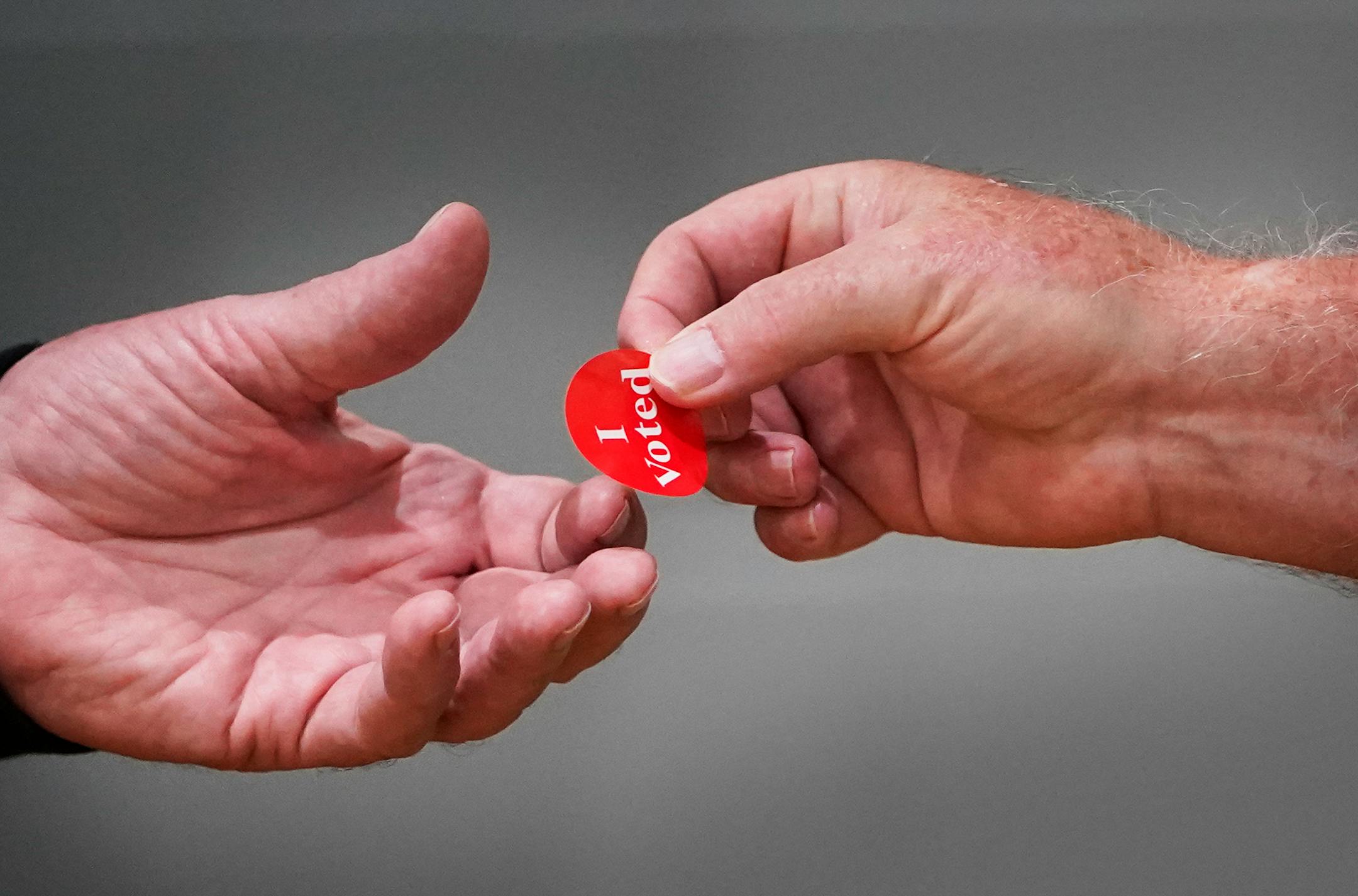 An election worker hands a voting sticker to a voter at Powderhorn Park during the primary election that includes the 5th congressional district in Minneapolis.
