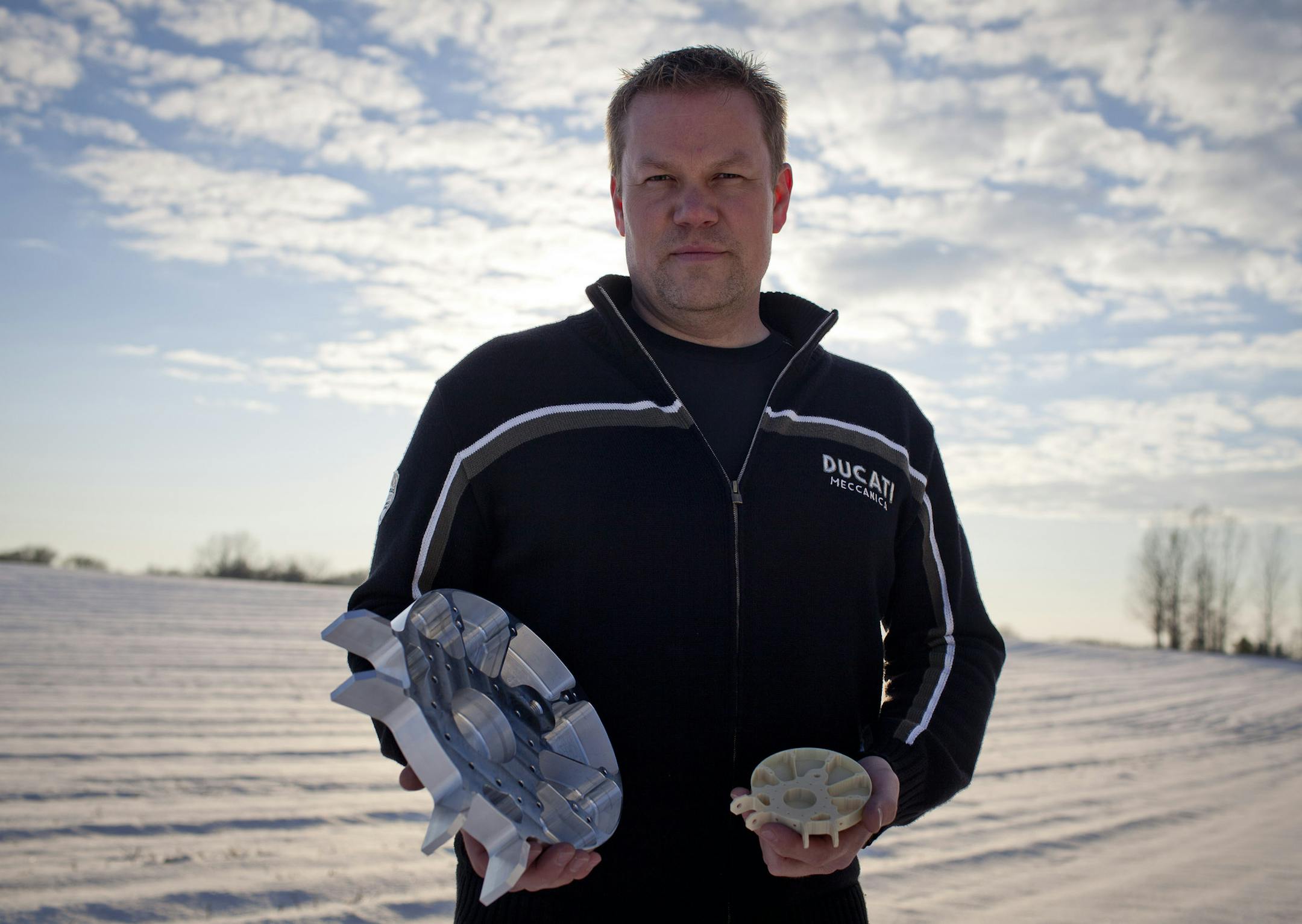 Jon Baklund, owner of Baklund R&D LLC, holds a 3D printed sample, right, and the Morpheus Mars landing craft foot manufactured by his company for NASA, as he stands for a photograph in a field outside the company's shop in Hutchinson, Minnesota, U.S., on Wednesday, Nov. 6, 2013. Baklund, which hired four people in the last year and is seeking two more, is one of hundreds of small shops across the U.S. leveraging technology to meet demand for low volume, highly-customizable products. Photographer