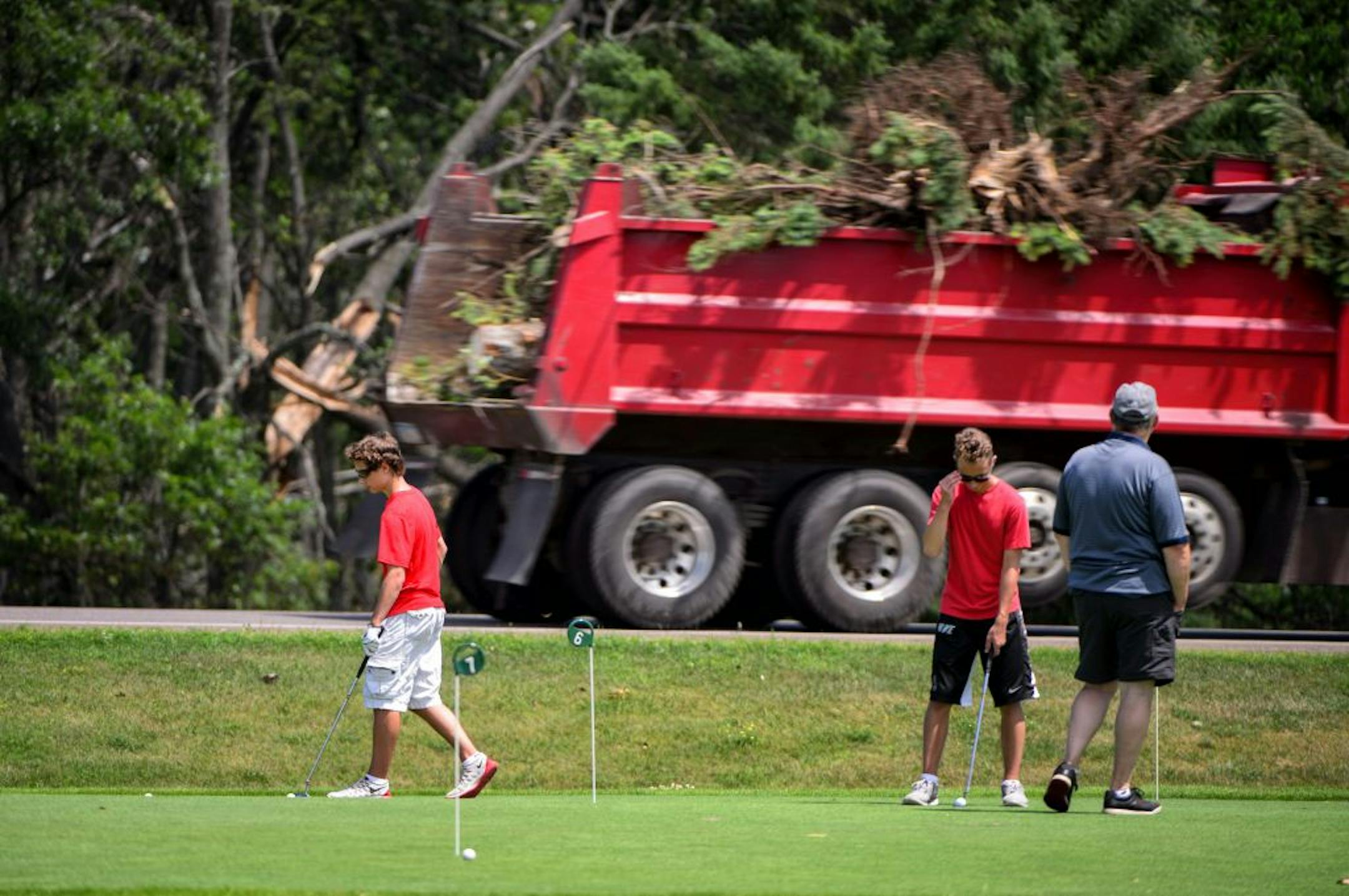 Charles Erickson and grandsons Drew and Alec, both 14, play golf on the putting green at Madden's resort in Nisswa, Minn., as a truck hauls storm damaged trees behind them on Friday, July 17, 2015. (Glen Stubbe/Star Tribune via AP) ST. PAUL PIONEER PRESS OUT; MAGS OUT; TWIN CITIES LOCAL TELEVISION OUT; MANDATORY CREDIT