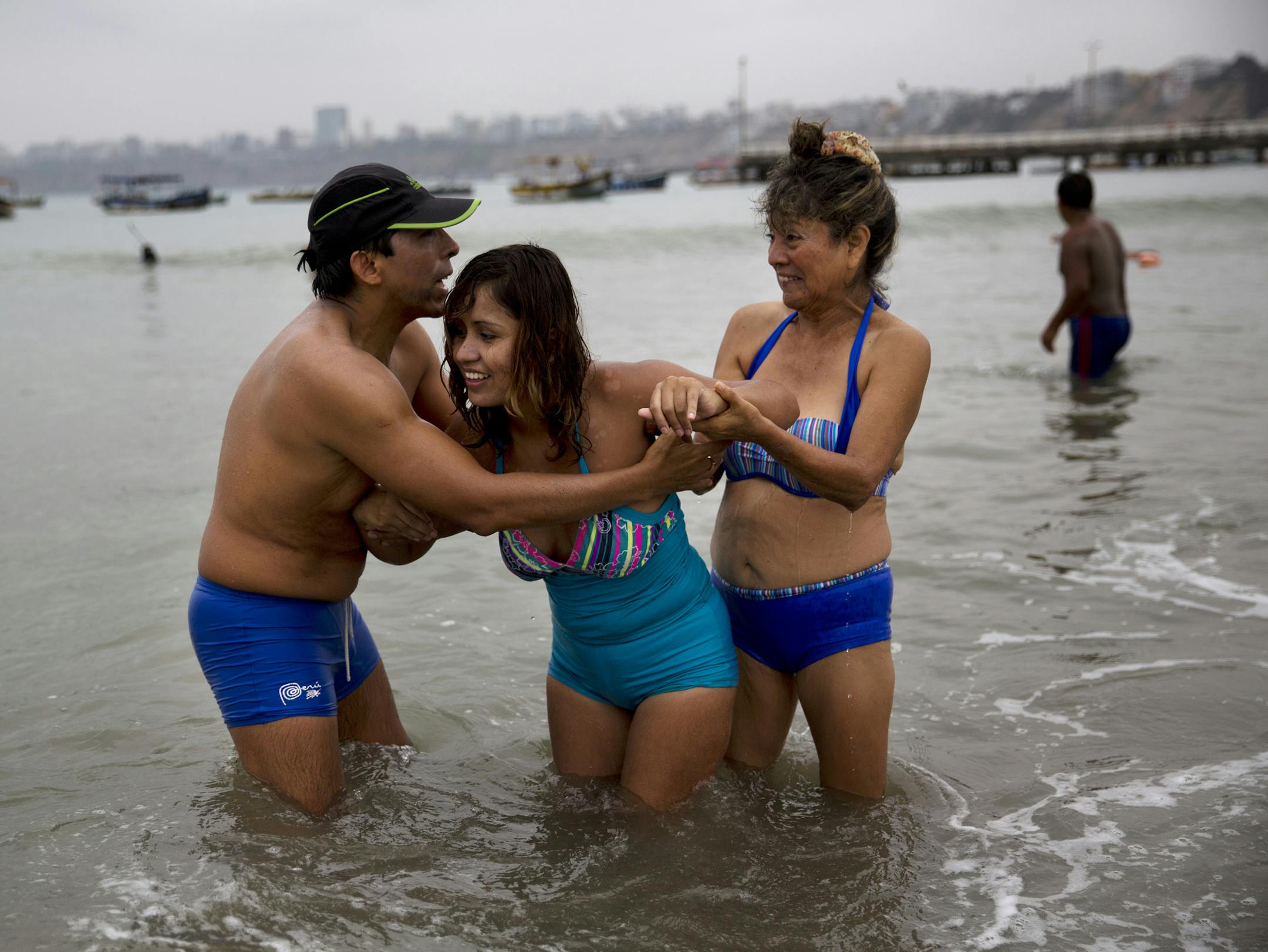 In this May 8, 2015 photo, friends help Gisela Sanchez who suffers rheumatoid arthritis walk in the water off Fishermen's Beach in Lima, Peru. “The sand calms the inflammation in my joints and the sea gives me tranquility,” said Sanchez, who traveled here from Patapo, a village at the foot of the Andes mountains about 700 kilometers (1,690 miles) north of Lima. Sanchez, 25, says she hasn't been able to walk on her own for the past four years, and that she's hoping the sea will help