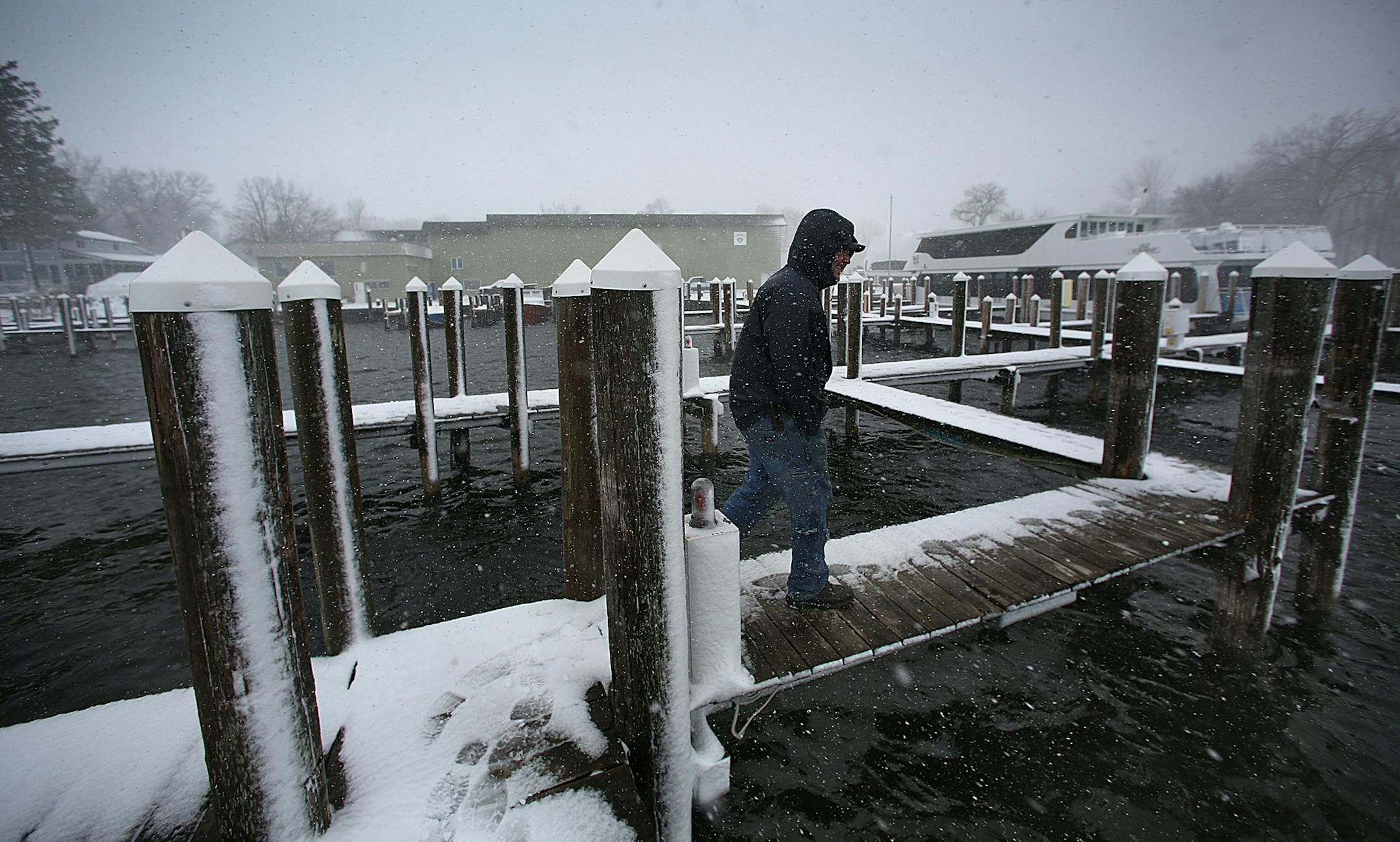 Snow fell atop docks and the shoreline at Tonka Bay Marina, where late-season ice on Lake Minnetonka has delayed many activities, including recreational boating, until warmer weather prevails. Last year the ice went out on the lake on March 21. This year several events have already been postponed, including the annual Lions Club crappie contest, which had been scheduled for this Saturday (April 20). Marine Technician Joe Determan carefully walked along the docks, having been assigned to ensure t
