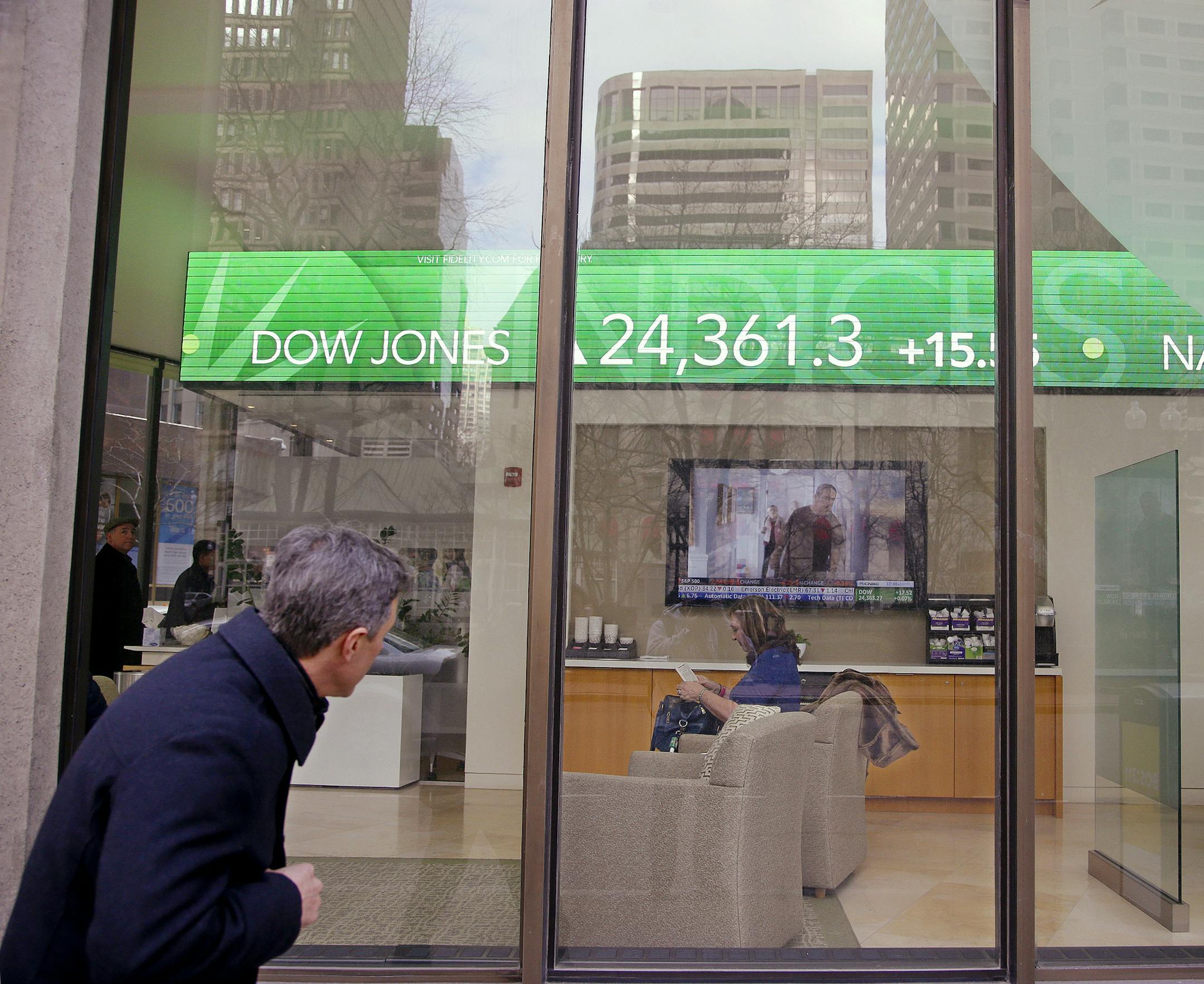 FILE- In this Feb. 6, 2018, file photo, a passer-by peers in the window while investors congregate inside at the Fidelity Investments office on Congress Street as the ticker displays stock market numbers in Boston. A plunge in stock prices always stings, but this recent one dug deeper because more of the country has become exposed to the ups and downs of the market, particularly older Americans. (AP Photo/Stephan Savoia, File)
