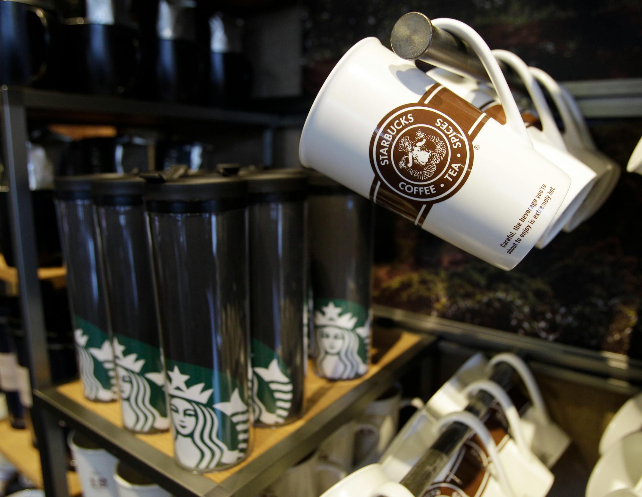 A mug with the original Starbucks Corp. logo is shown at upper right, Tuesday, March 8, 2011, next to a rack of insulated cups bearing the company's new logo, at a Starbucks store in downtown Seattle, on the day marking the 40th anniversary of the company. The new logo drops the word "Starbucks," but still features the coffee company's signature "Siren" figure.